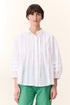 Model wearing white short sleeve shirt with frill detail on a white background paired with green pants 