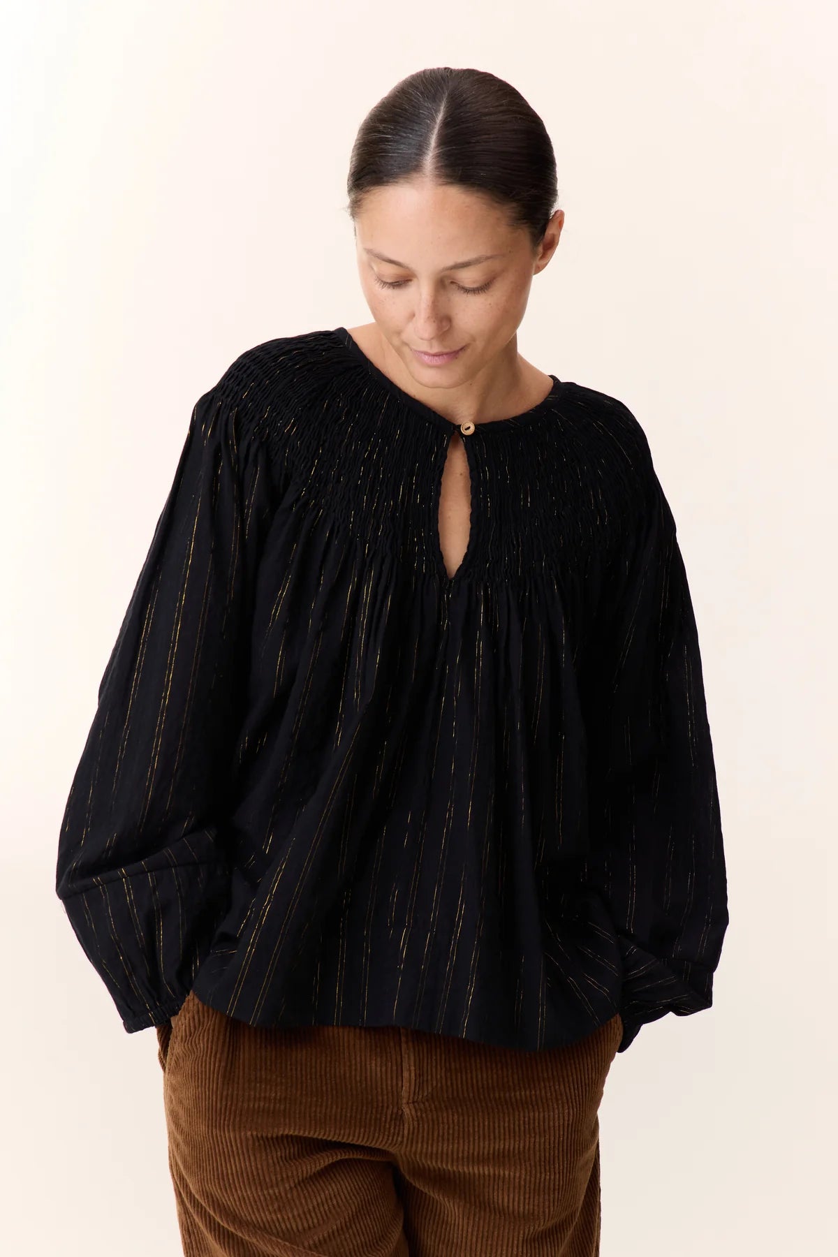 Women wearing a black shirt with gold vertical stripe detail on a white background. 