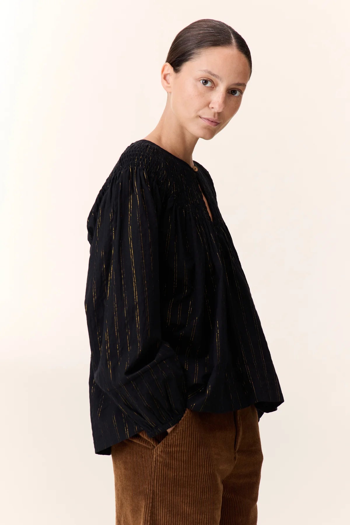 Women wearing a black shirt with gold vertical stripe detail on a white background. 