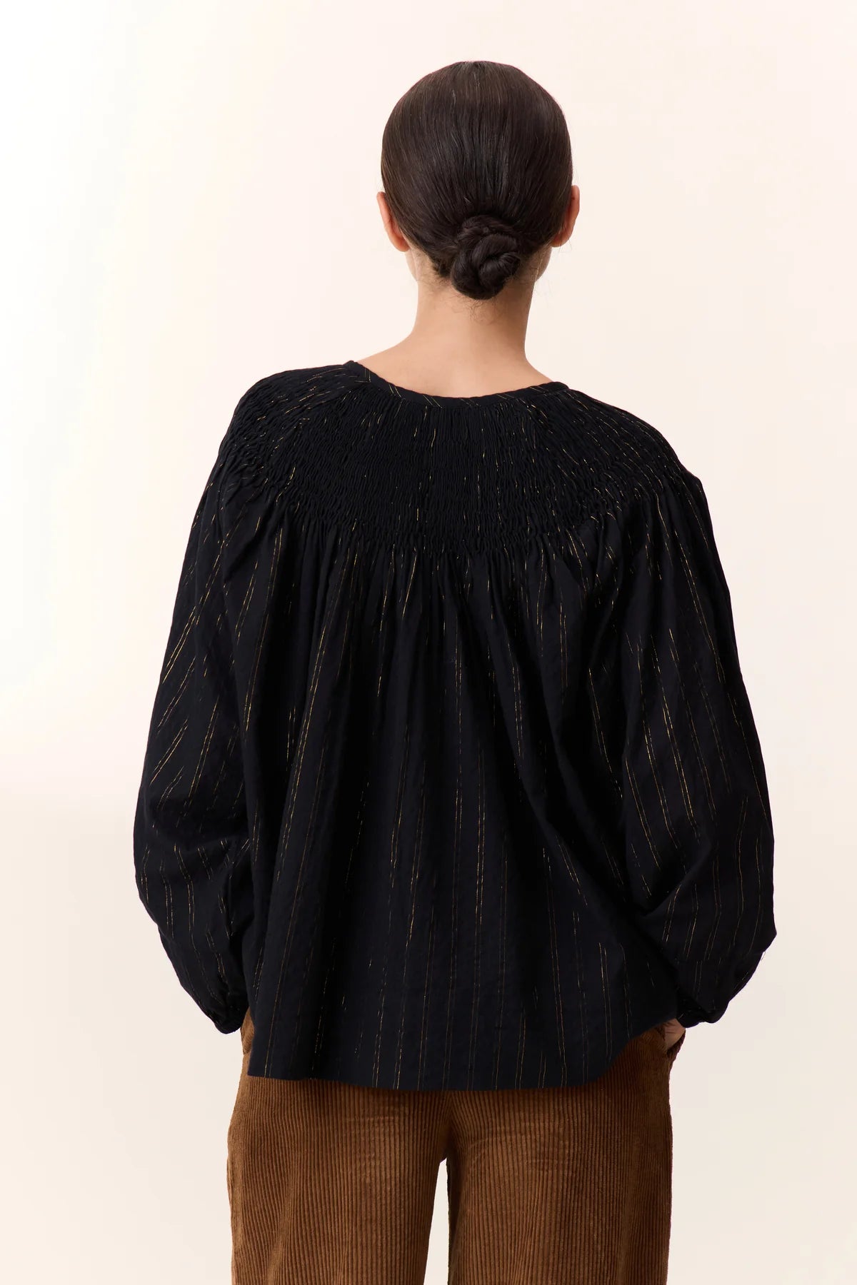 Women wearing a black shirt with gold vertical stripe detail on a white background. 