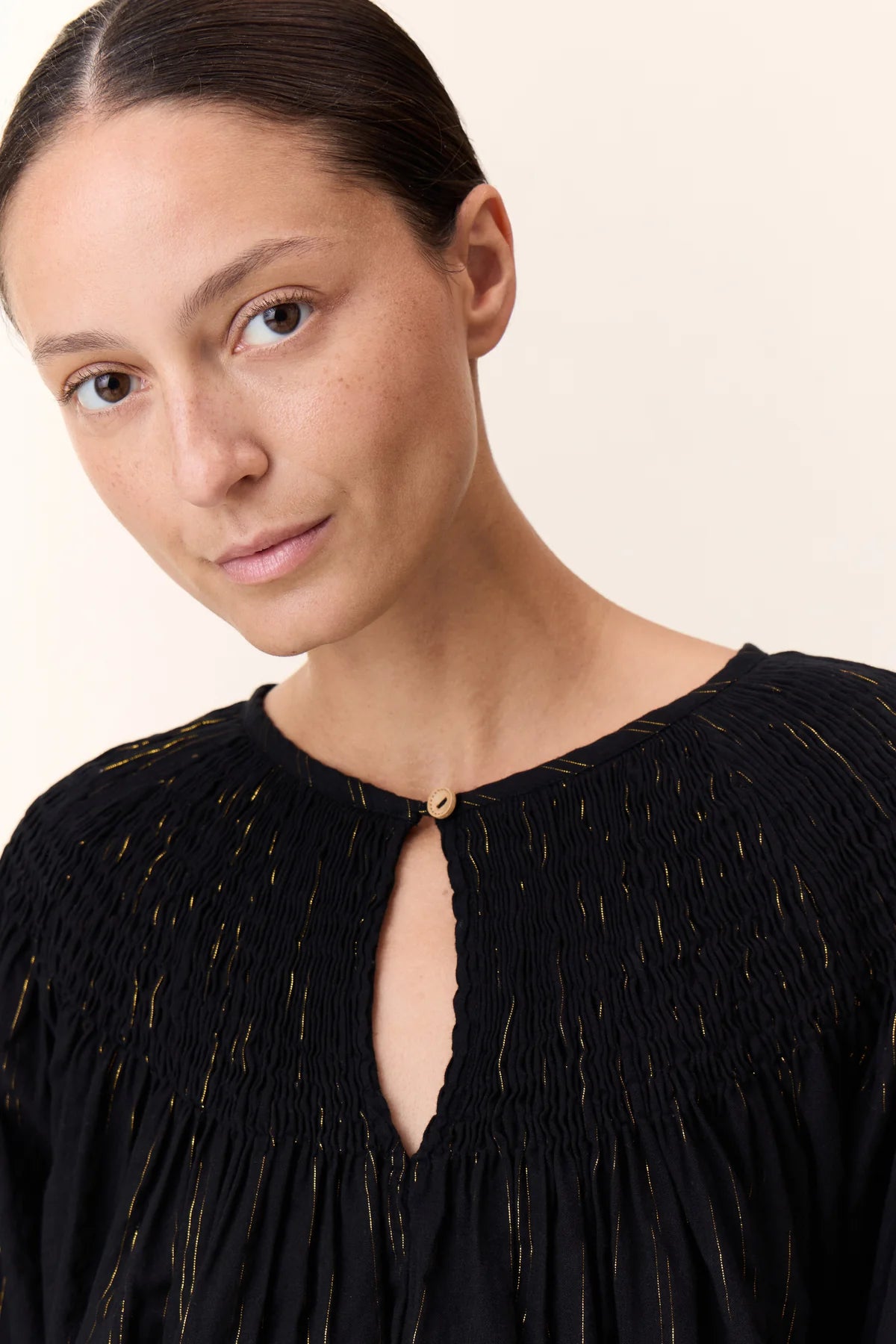 Women wearing a black shirt with gold vertical stripe detail on a white background. 