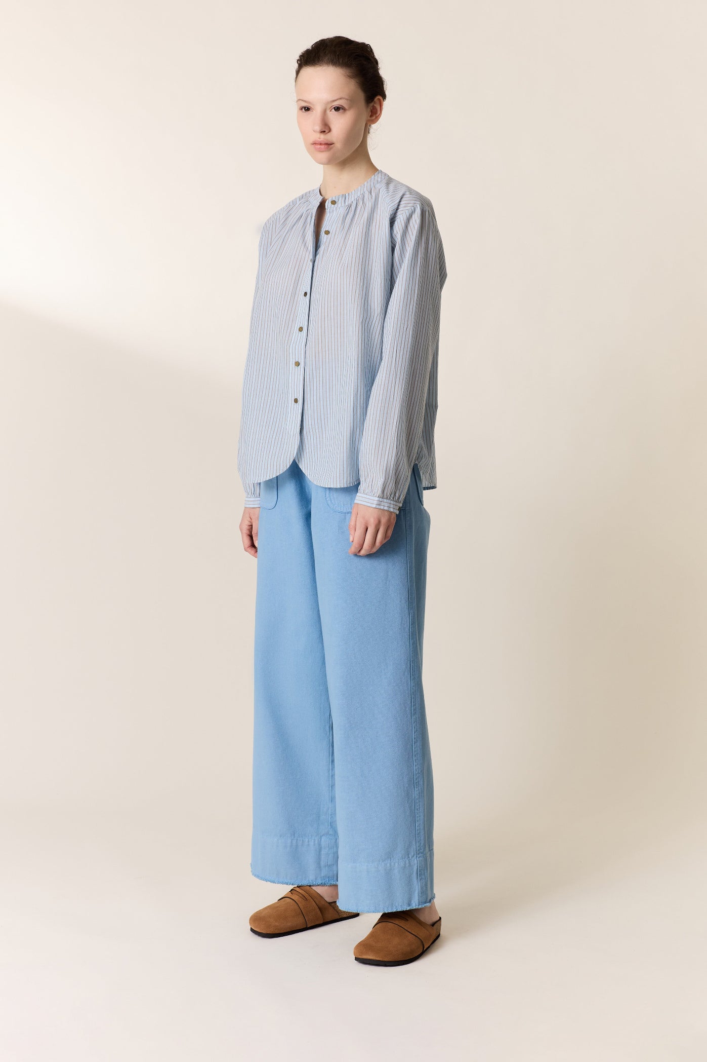 Women shown wearing a. blue stripe shirt and blue pants with tan slides on a plain background. 