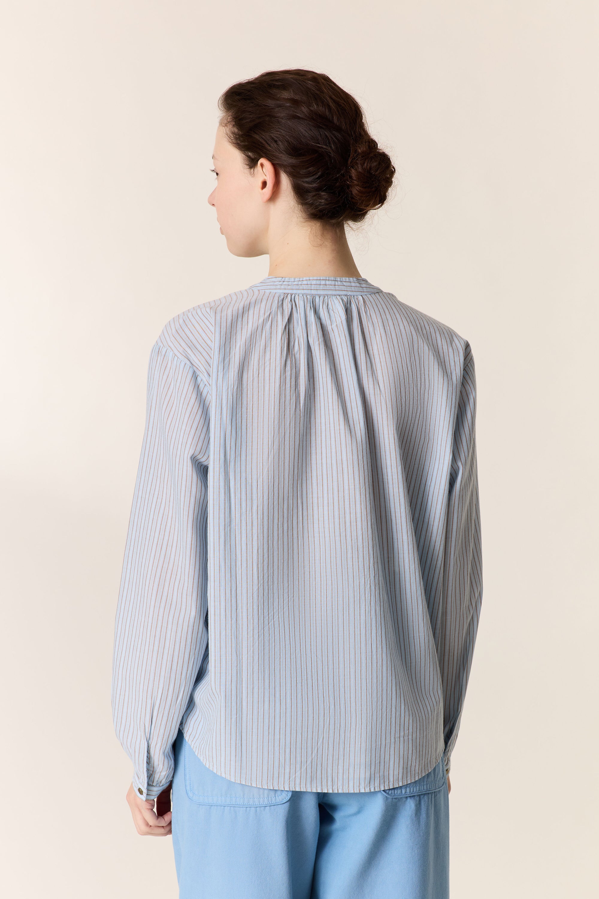Women shown from the back wearing a. blue stripe shirt and blue pants on a plain background. 