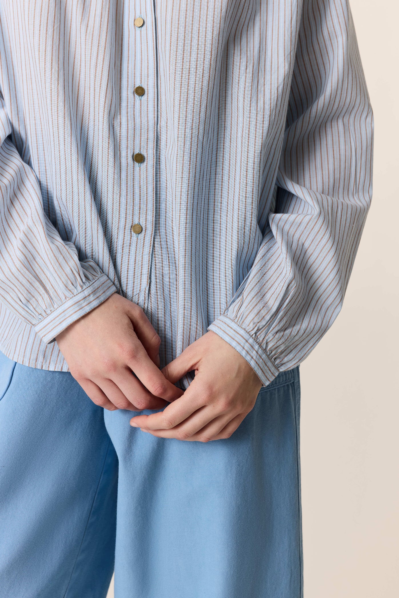 Women shown up close wearing a. blue stripe shirt and blue pants on a plain background. 