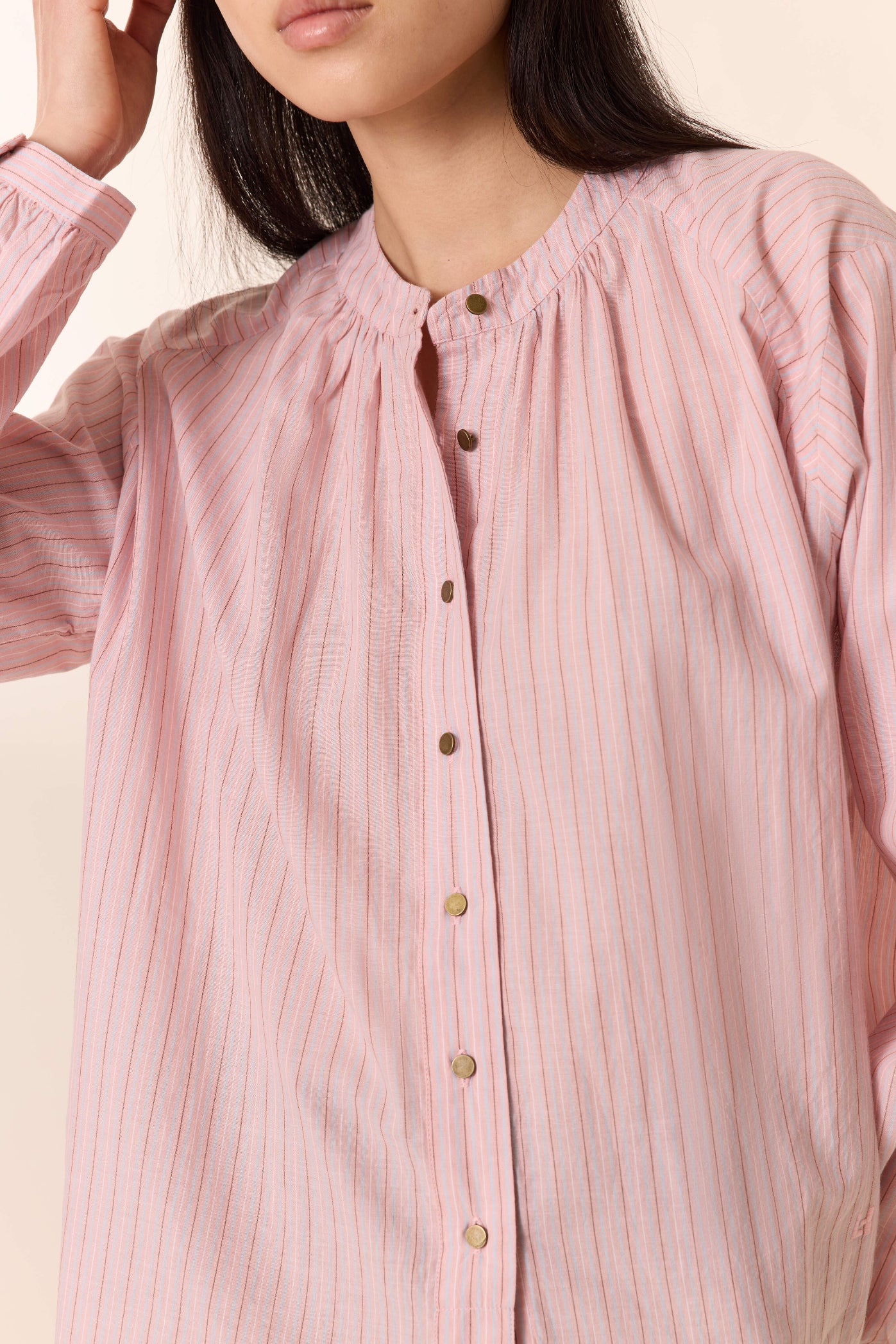 Close-up of a person wearing a pink striped shirt with gold buttons on a light background