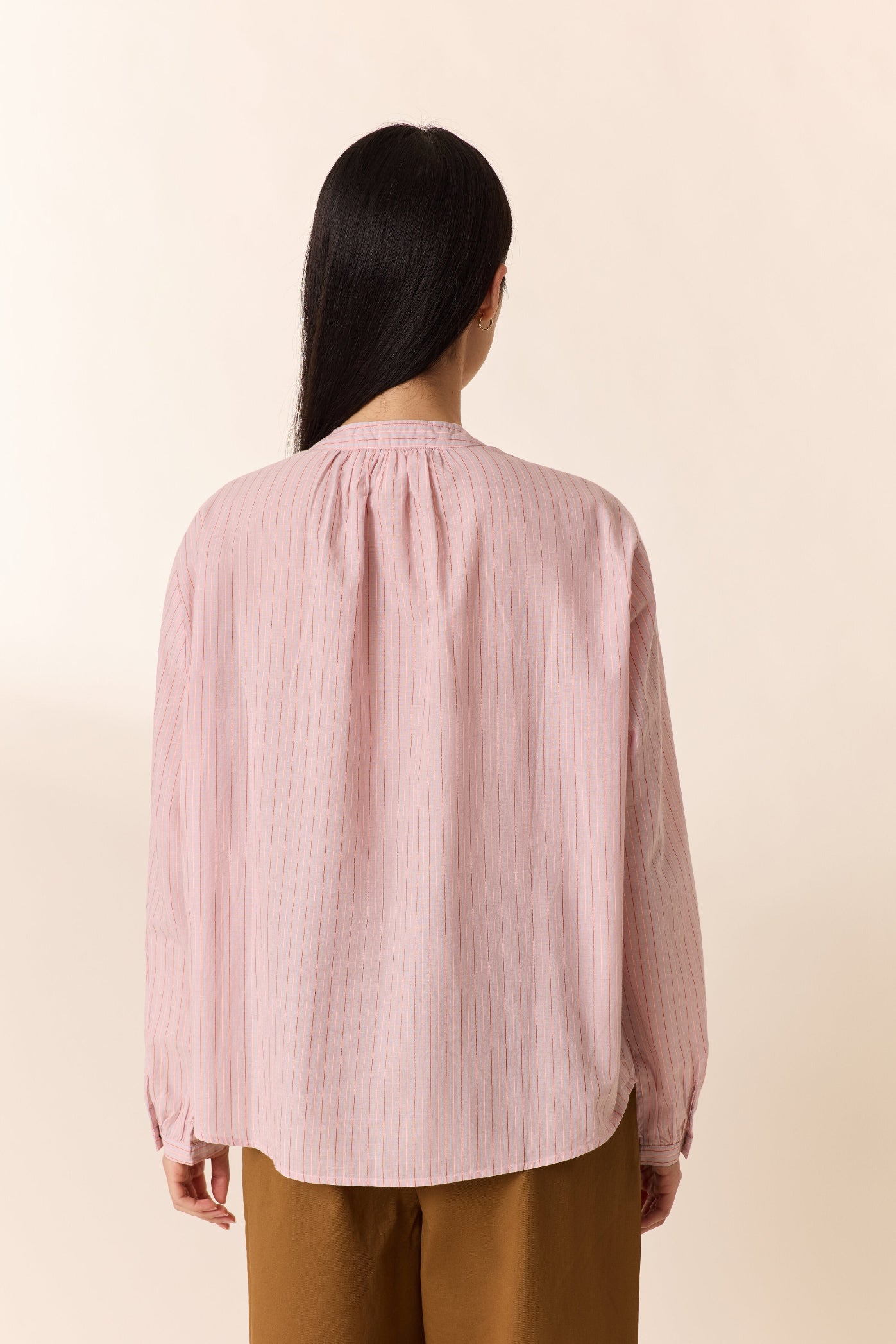 Person wearing a light pink blouse with long sleeves on a beige background