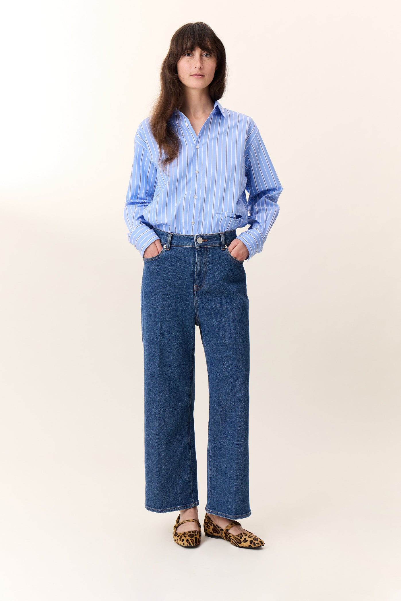 Woman wearing a light blue striped shirt and blue jeans on a white background