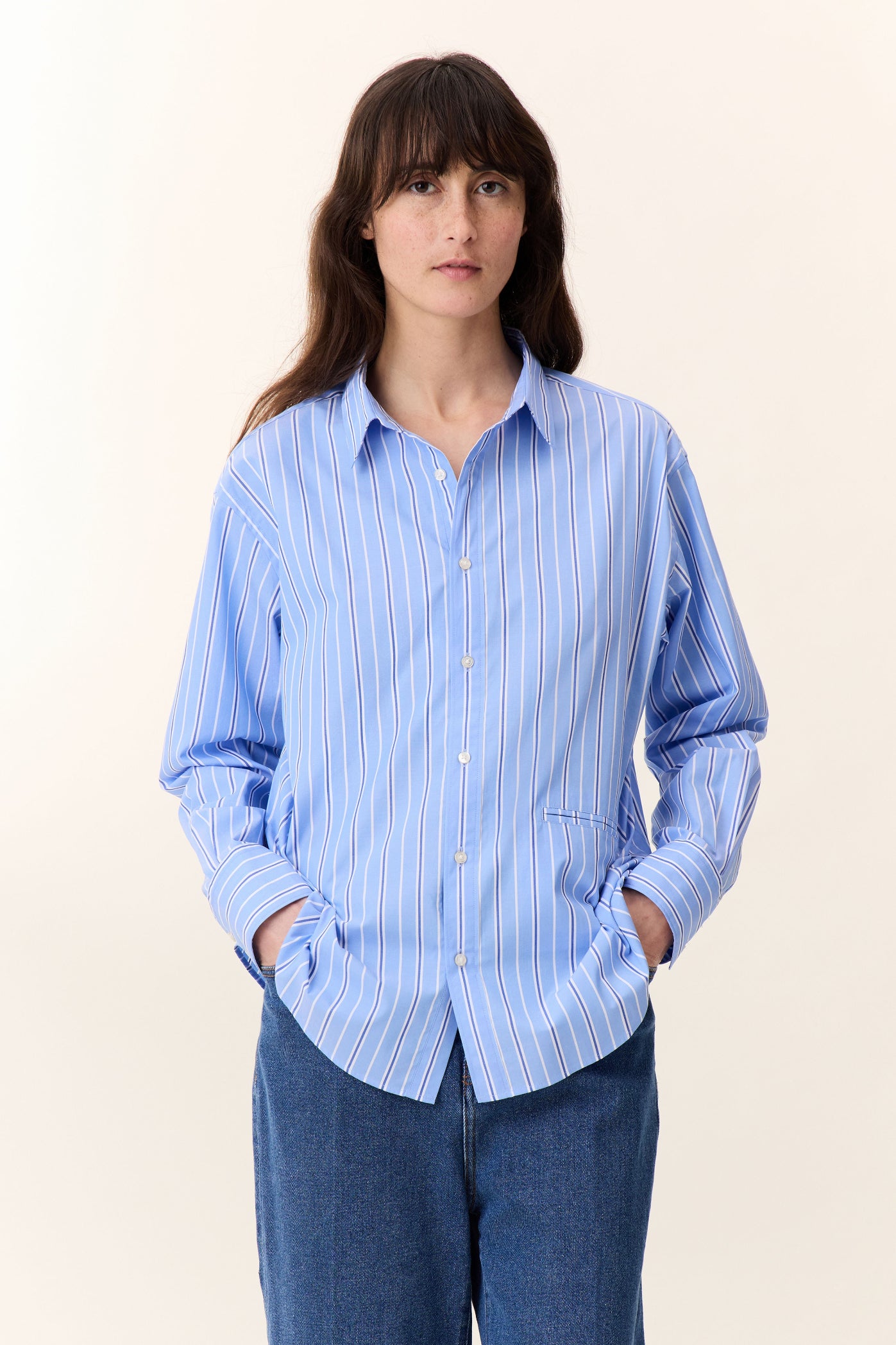 Woman wearing a light blue striped shirt and blue jeans on a white background