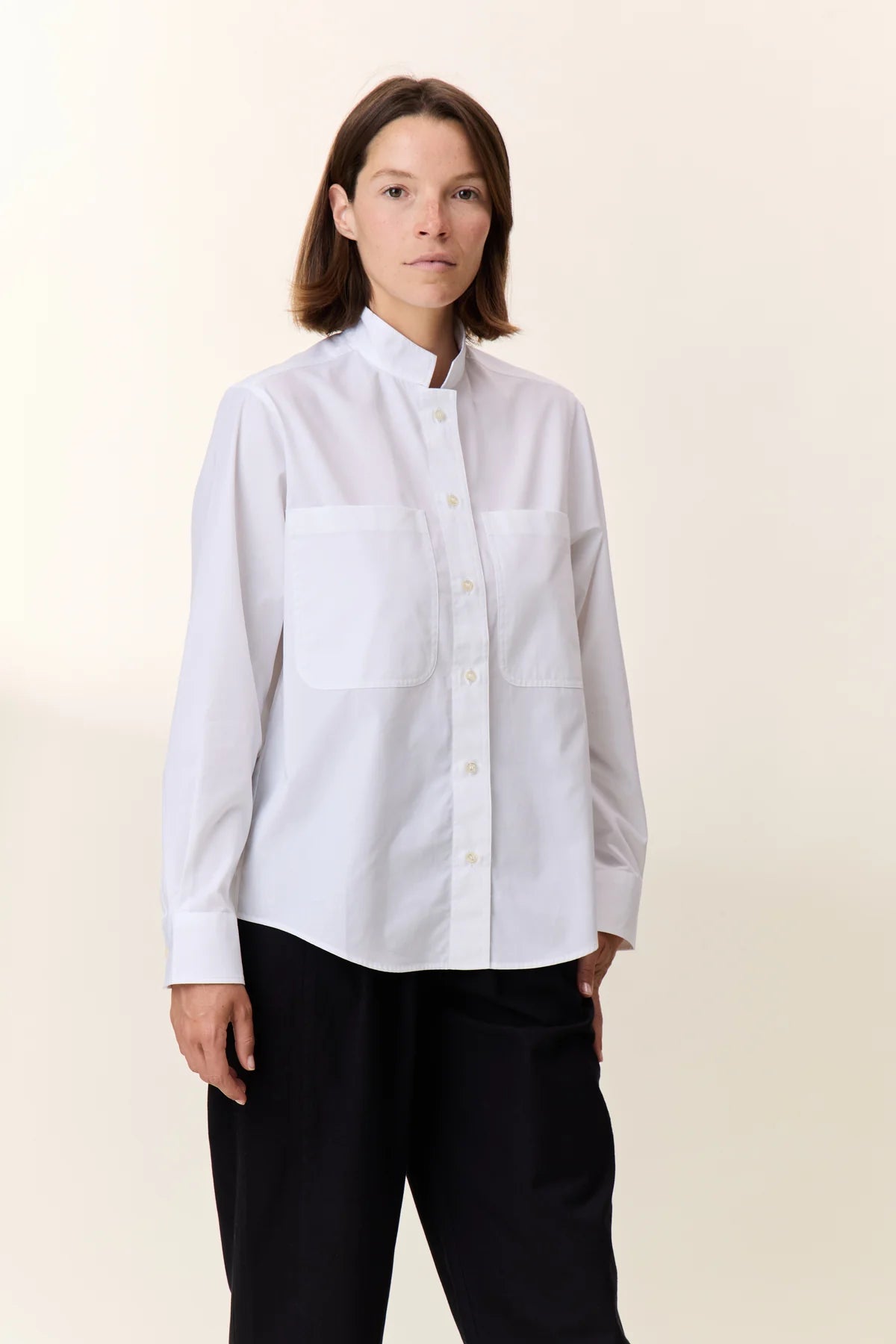 Person wearing a white shirt with mandarin collar and black pants on a beige background