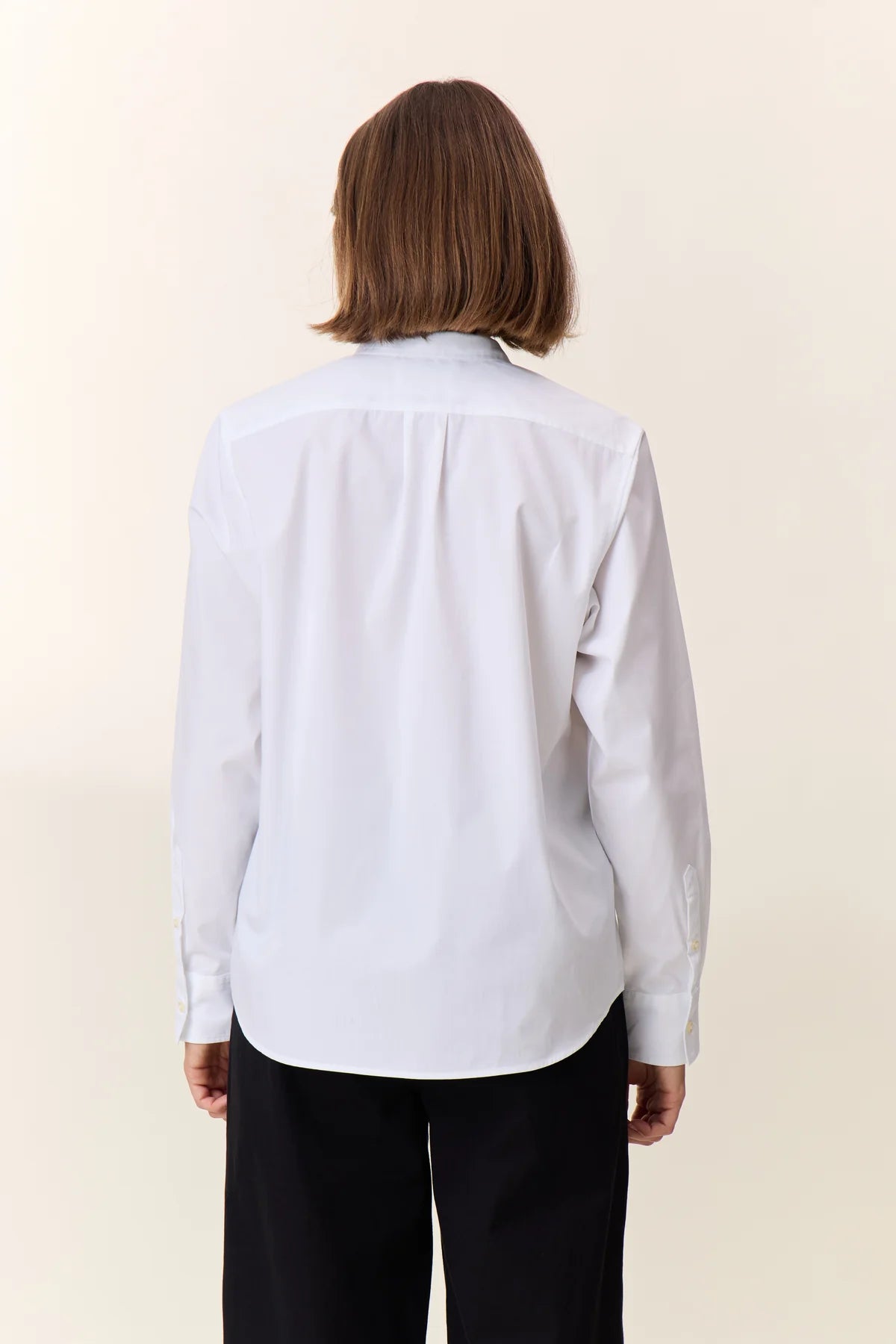 Person wearing a white shirt with Mandarin collar and black pants showing back of shirt on a beige background