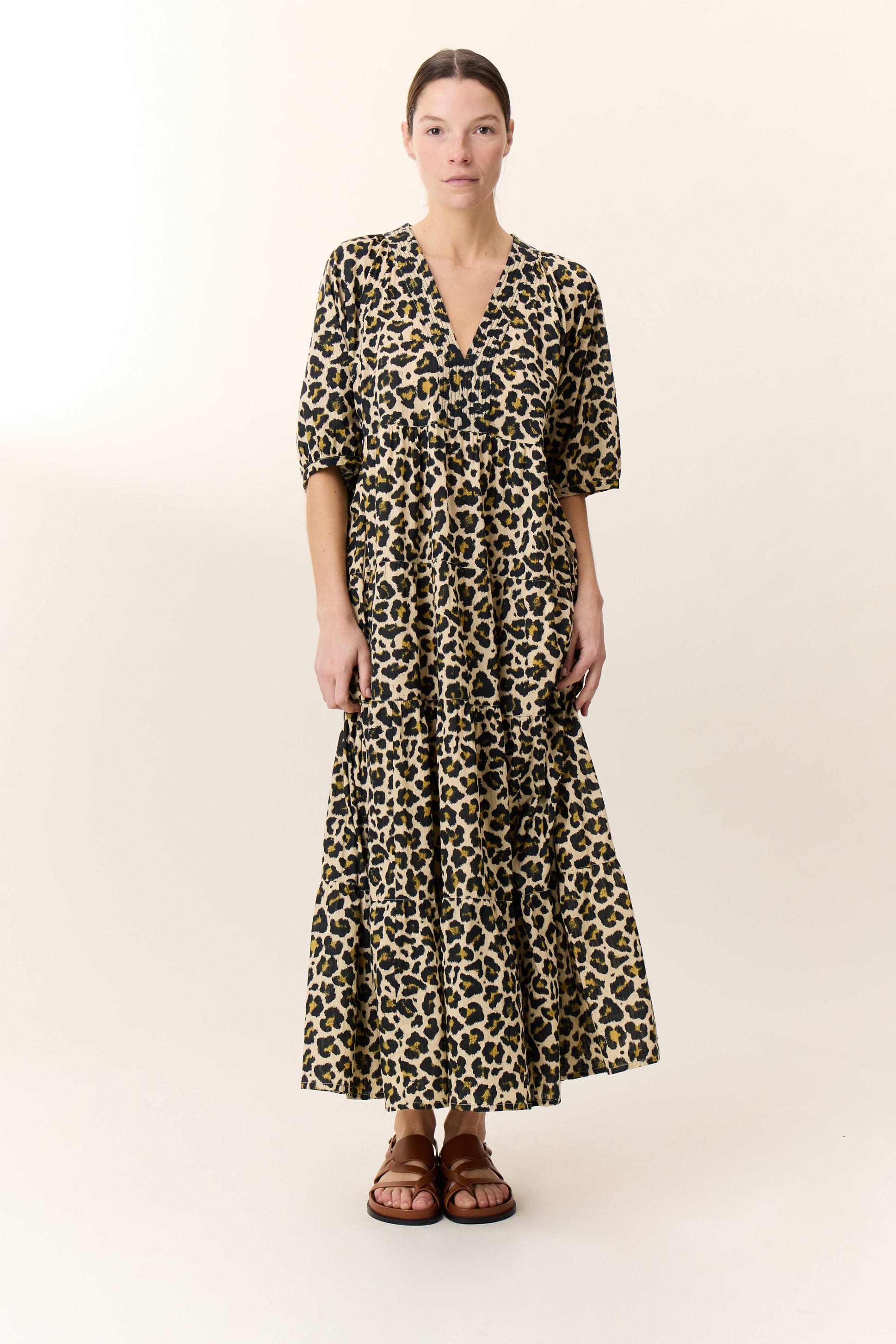 Woman wearing a maxi leopard print dress with tan sandals on a white background