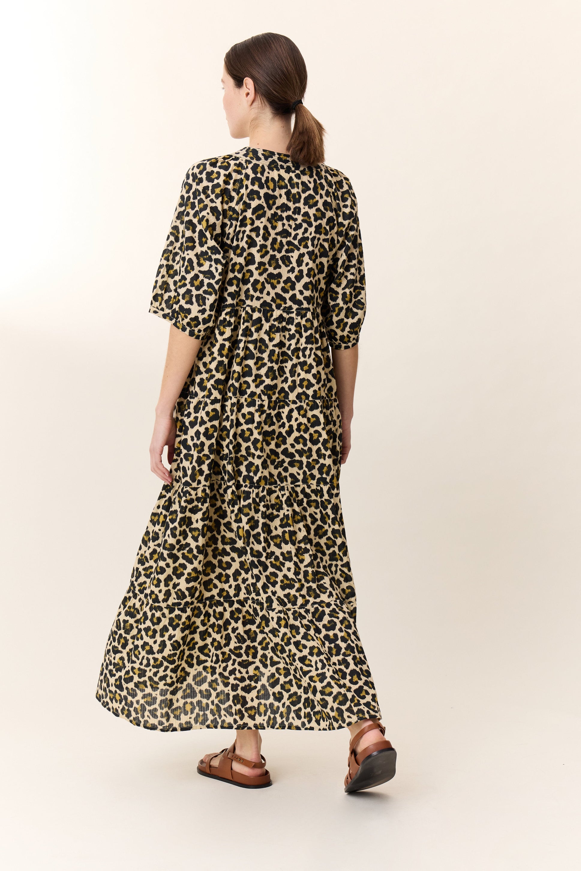 Woman wearing a maxi leopard print dress with tan sandals on a white background