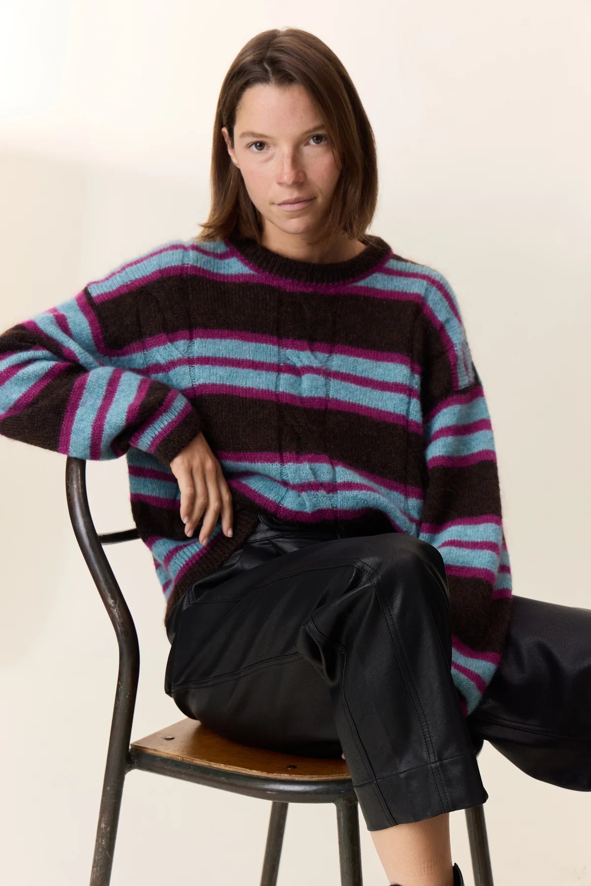 Person wearing a striped sweater sitting on a chair against a plain background