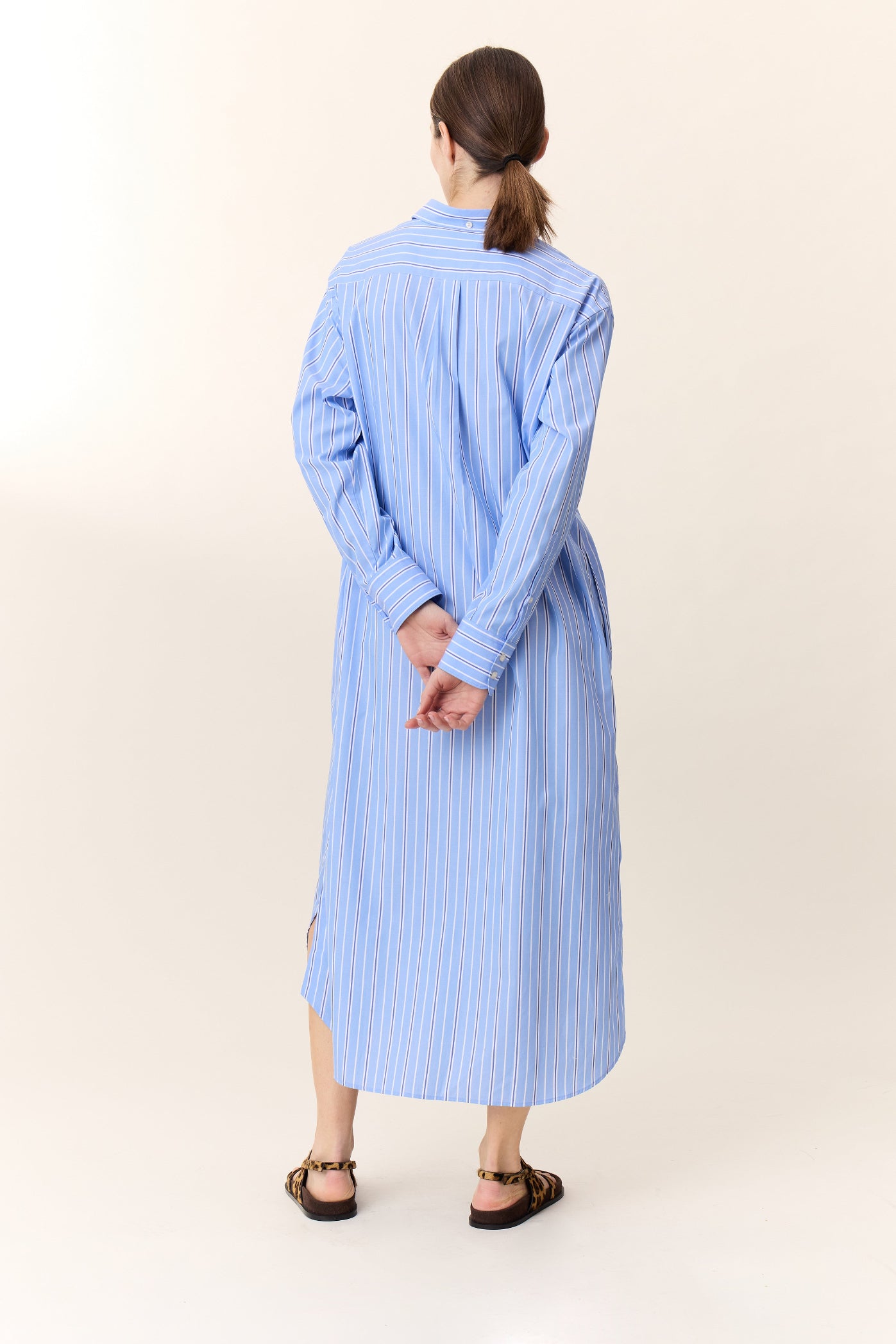 Model wearing long sleeve blue striped shirt dress with leopard print sandals on a white background. 