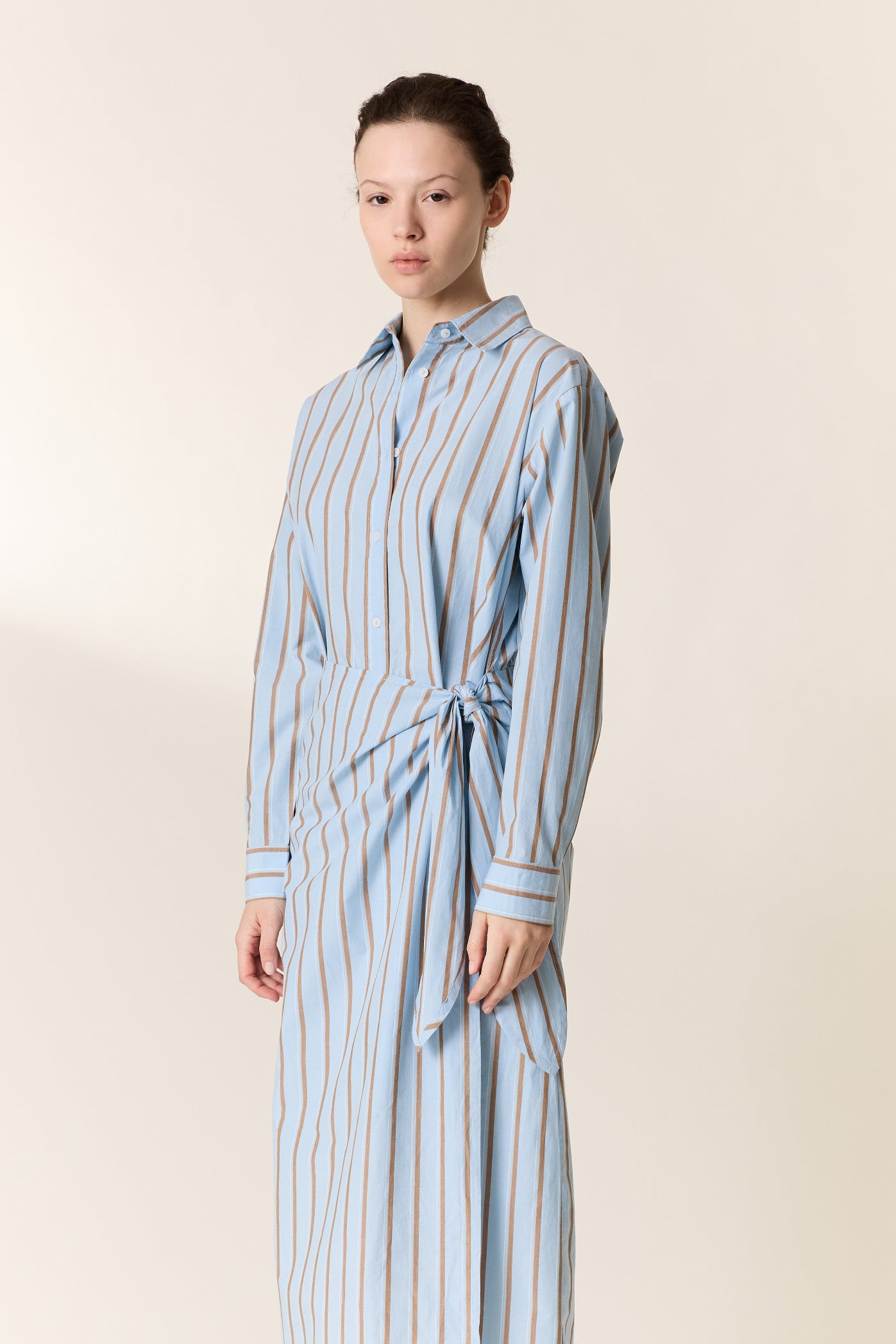 Woman wearing a light blue and white striped dress against a beige background
