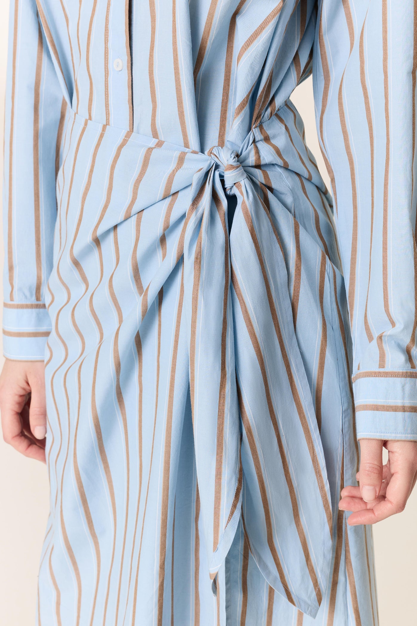Light blue and beige striped dress with a tie waist on a neutral background
