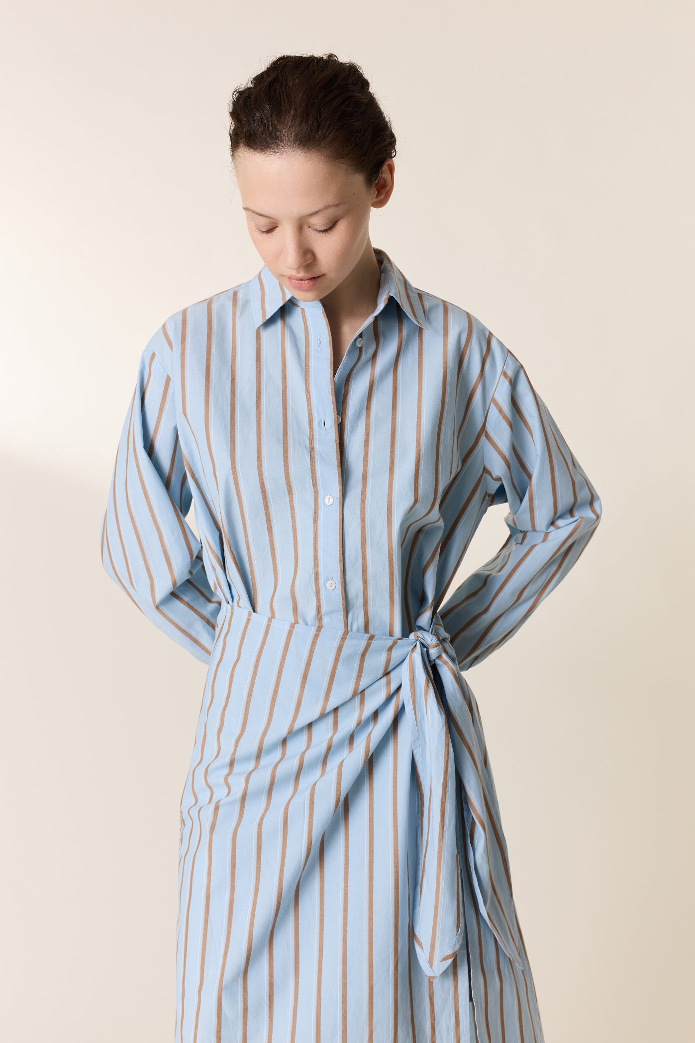 Woman wearing a blue and white striped dress against a beige background