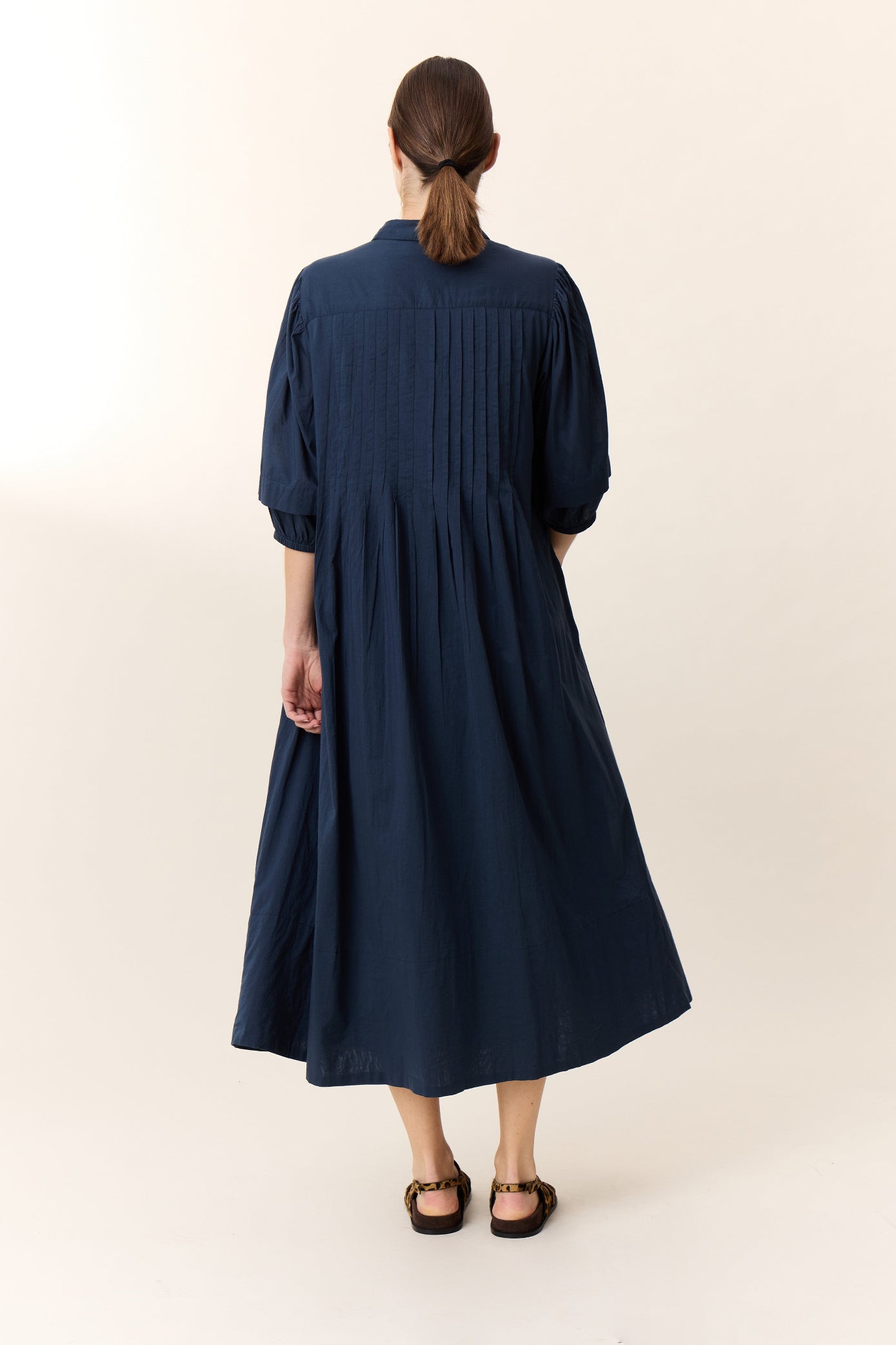 Model wearing midi dress in navy  with puff sleeves and frill detail on a white background