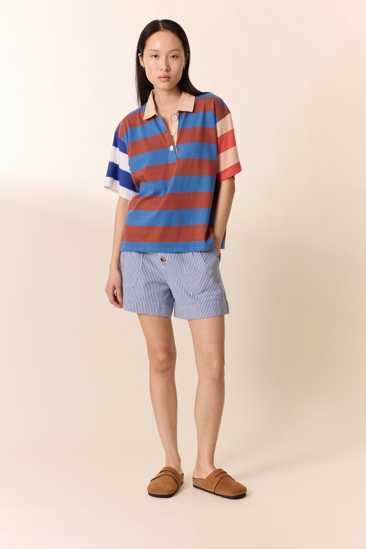 Woman wearing a striped polo shirt and shorts on a beige background