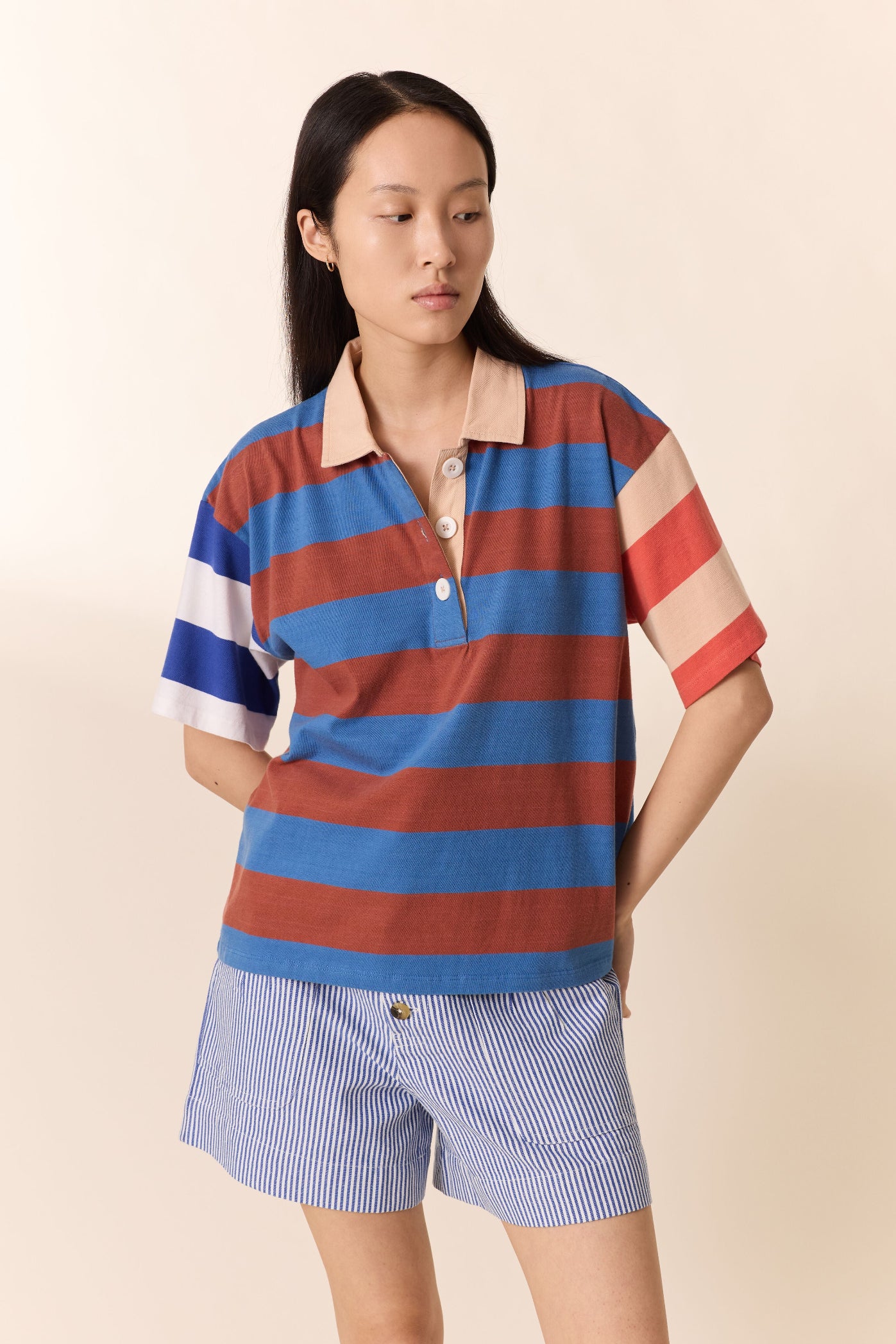 Woman wearing a striped polo shirt and shorts on a beige background
