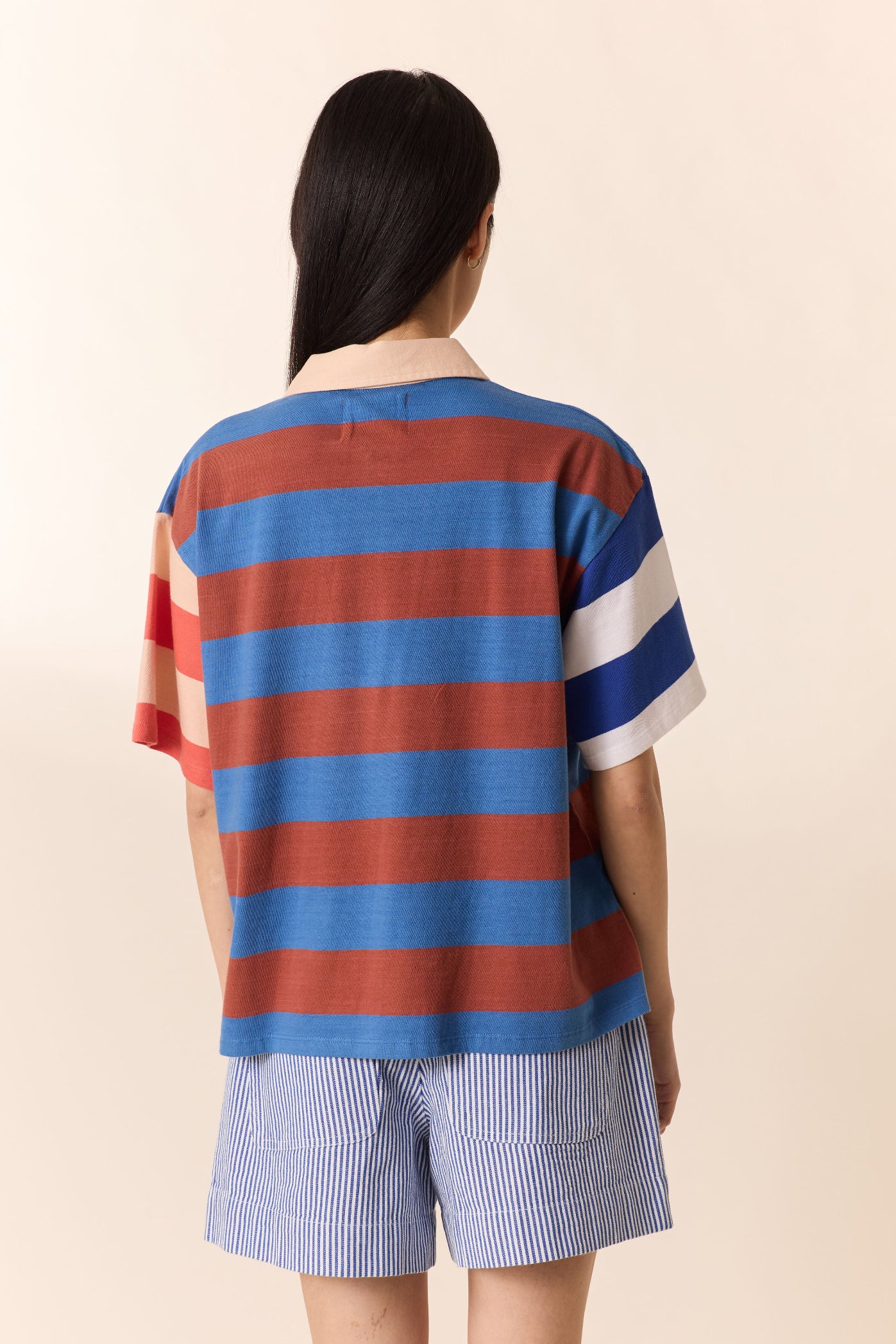 Person wearing a striped shirt and shorts against a beige background
