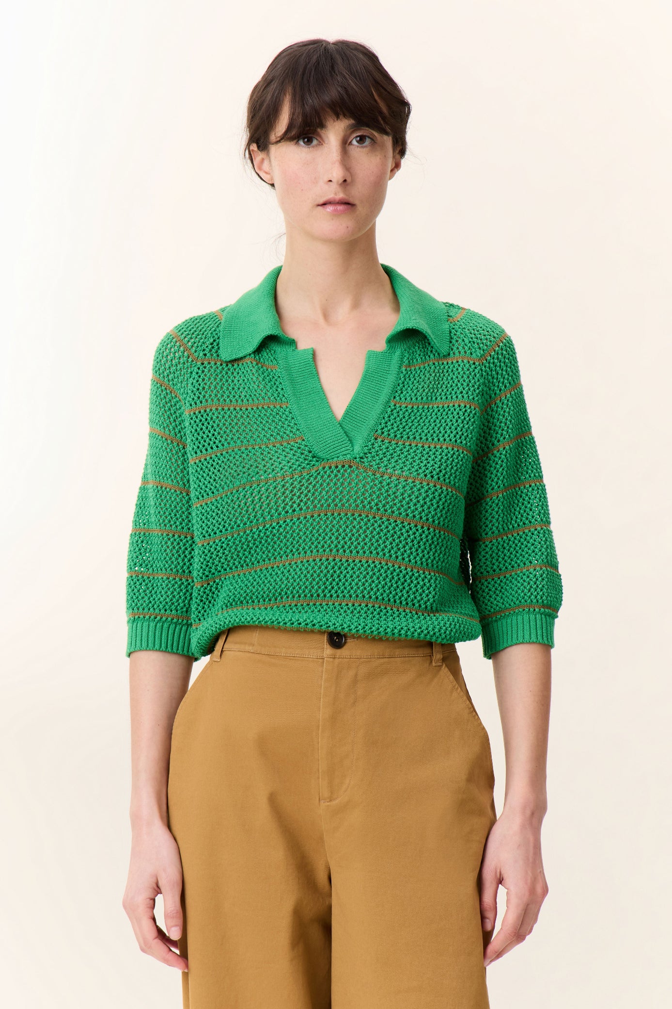 Woman wearing a green striped sweater and brown pants on a beige background