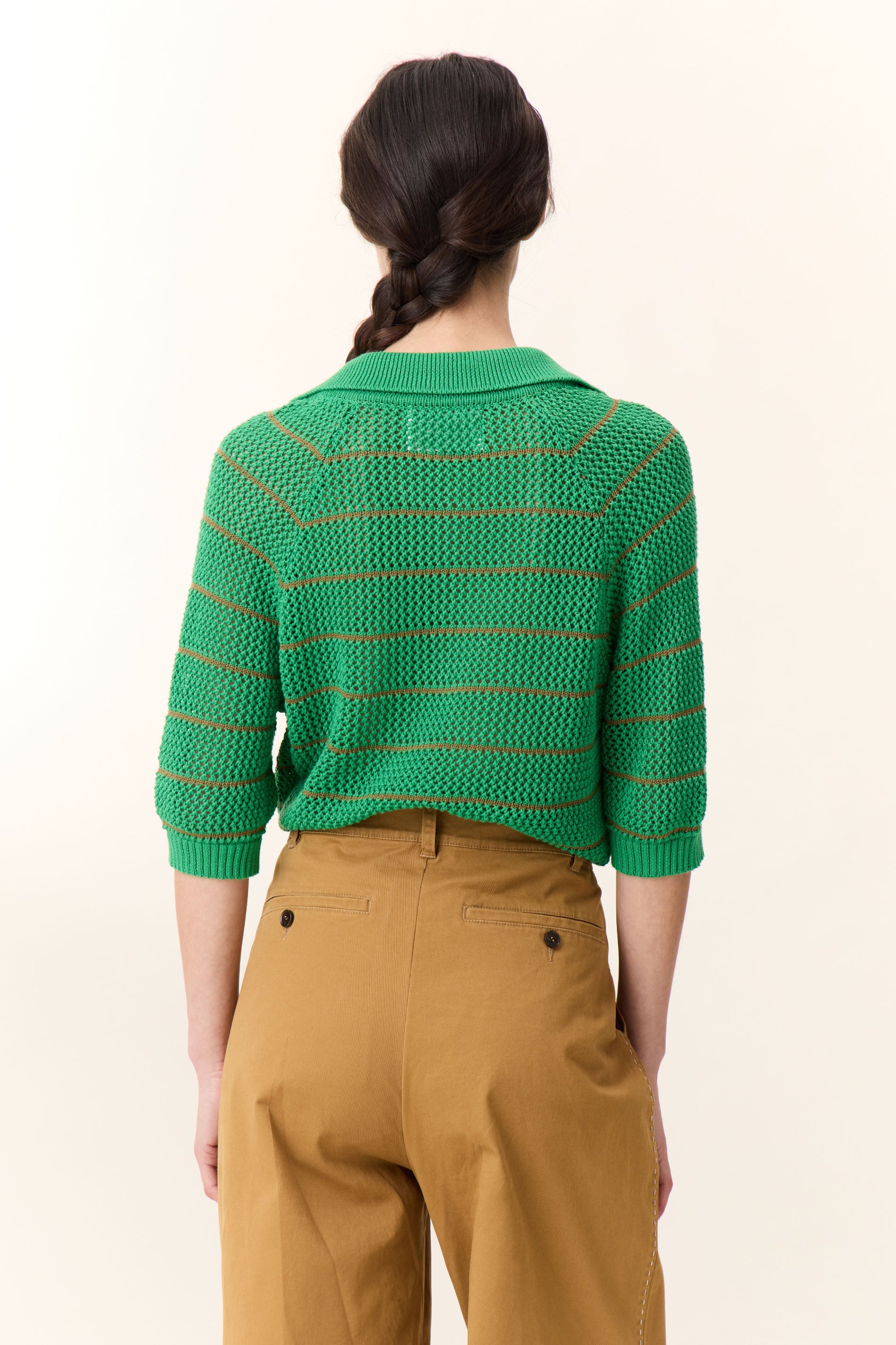 Person wearing a green striped sweater and brown pants on a white background