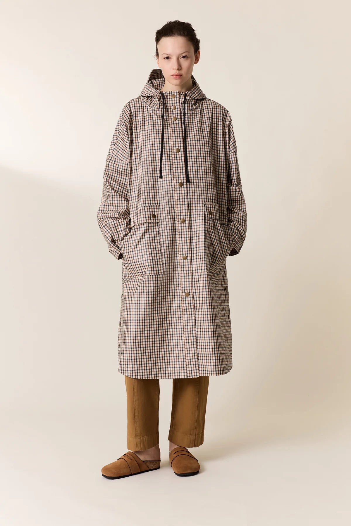 Person wearing a checkered raincoat and brown pants on a plain background