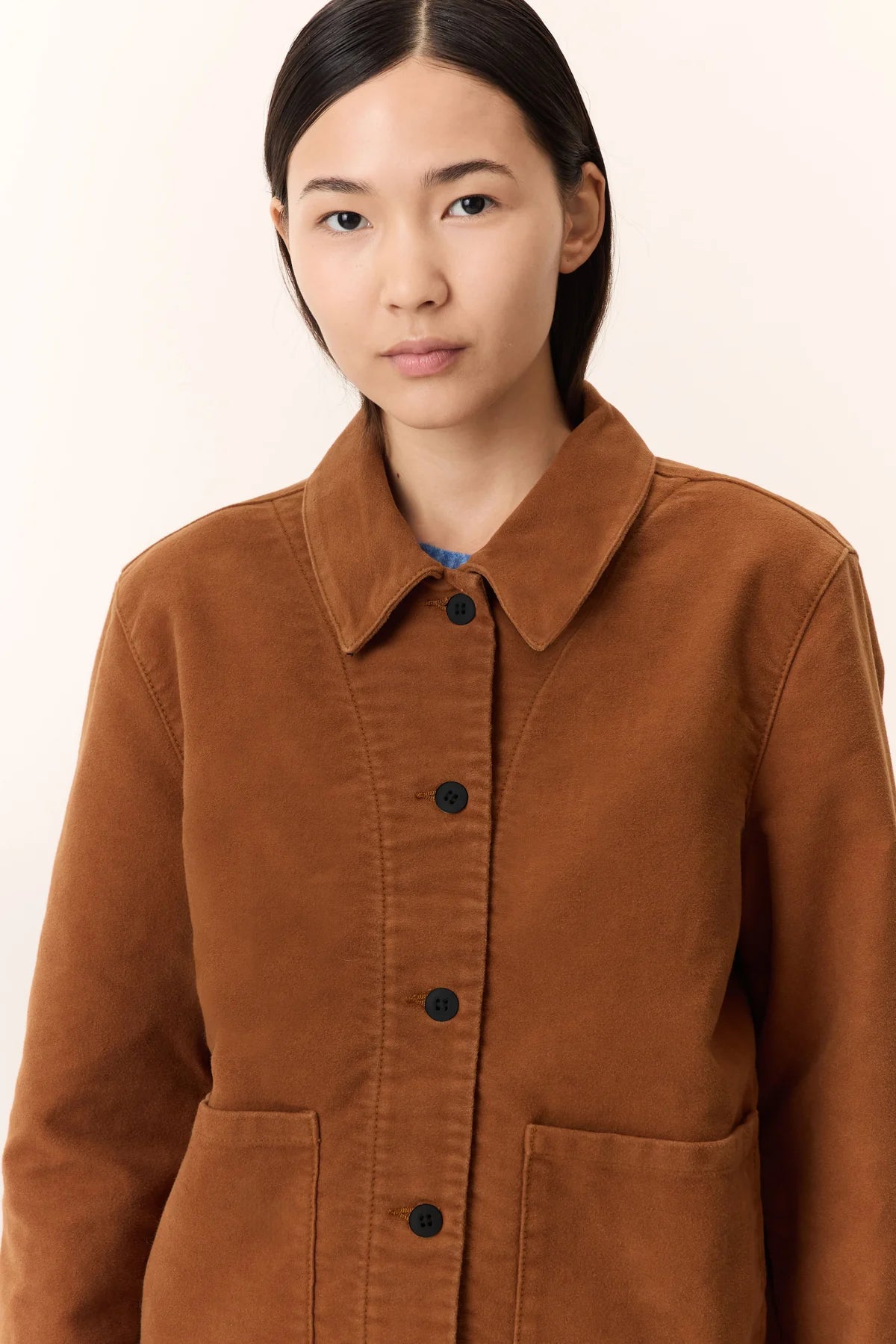 Woman wearing a camel brown jacket against a plain background
