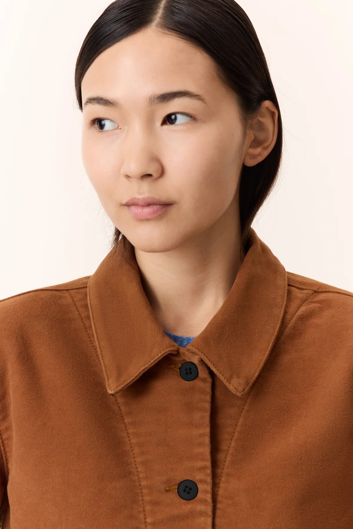 Person wearing a brown jacket with a plain background