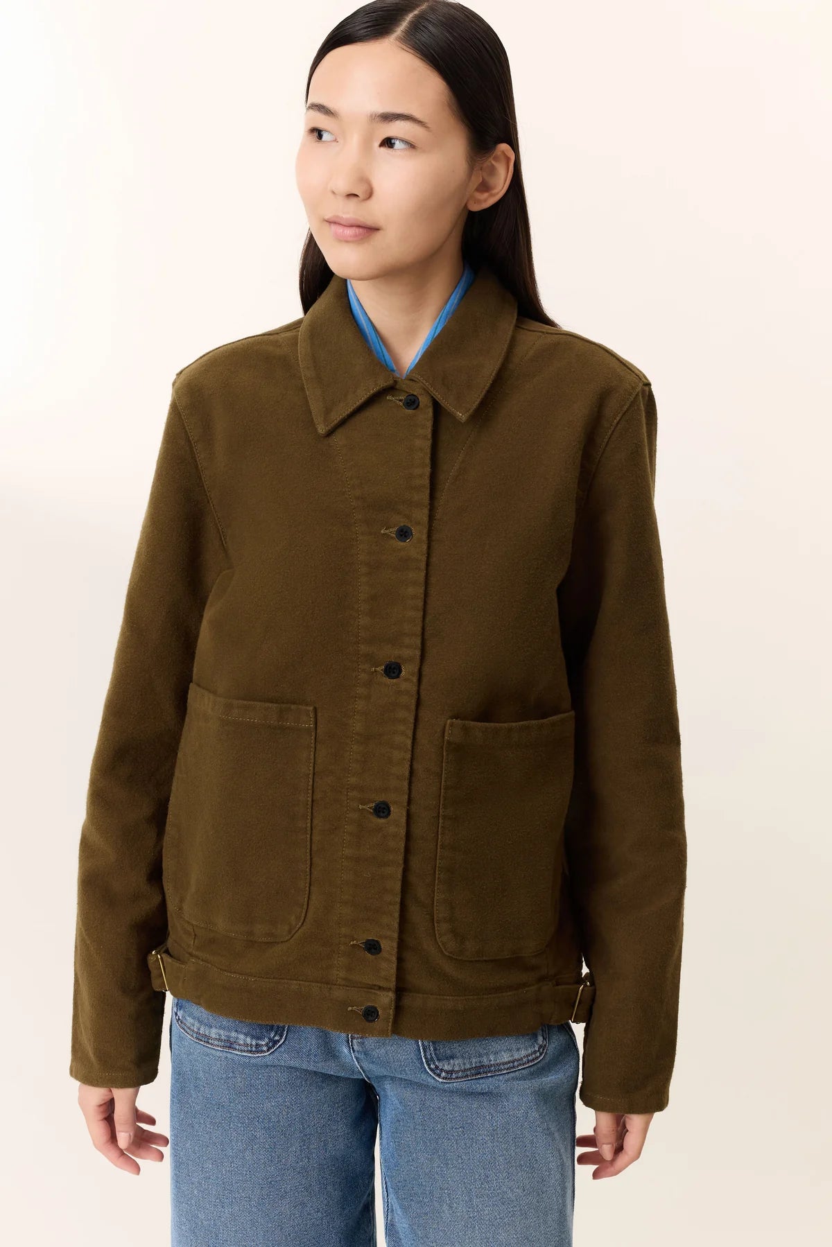 Person wearing a khaki jacket and blue jeans on a beige background