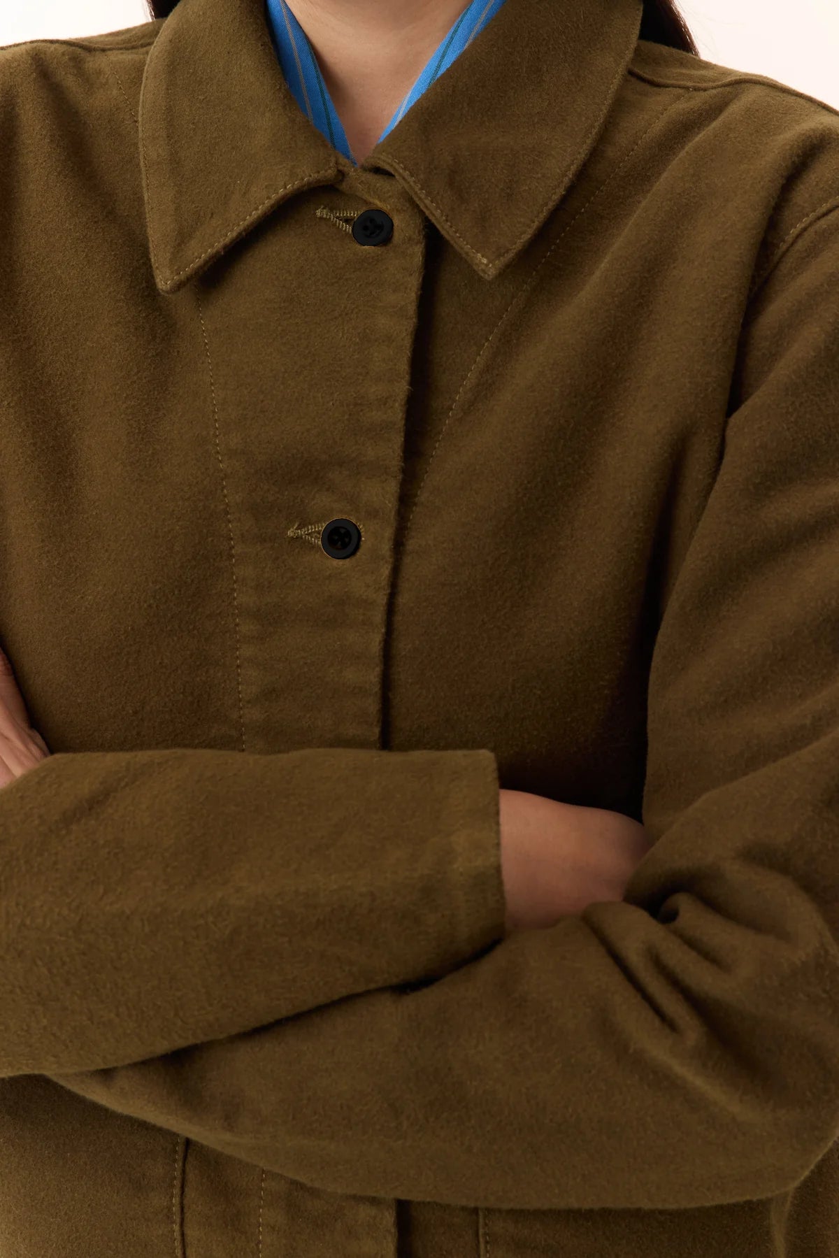 Person wearing a khaki jacket up colse to show buttons and collar a beige background