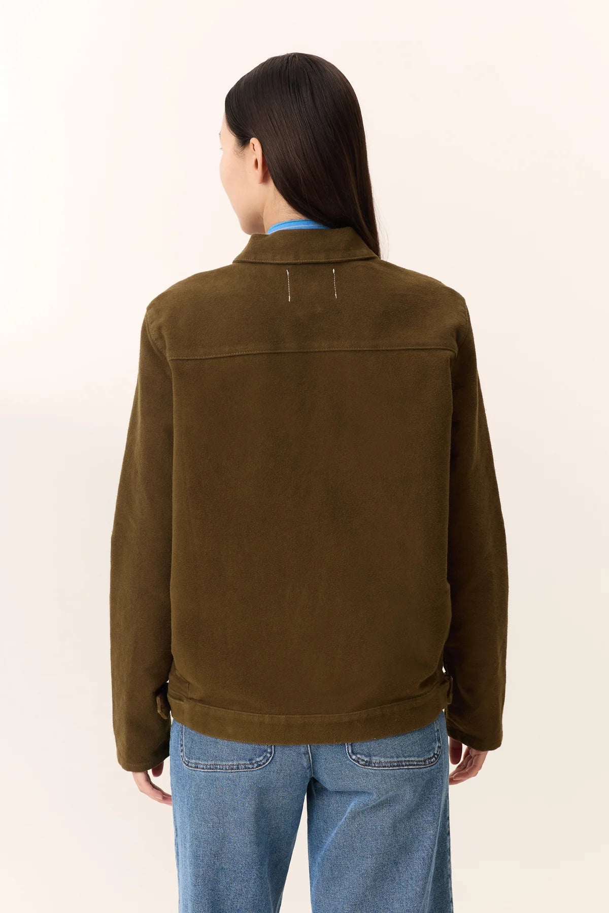 Person wearing a khaki jacket and blue jeans on a beige background