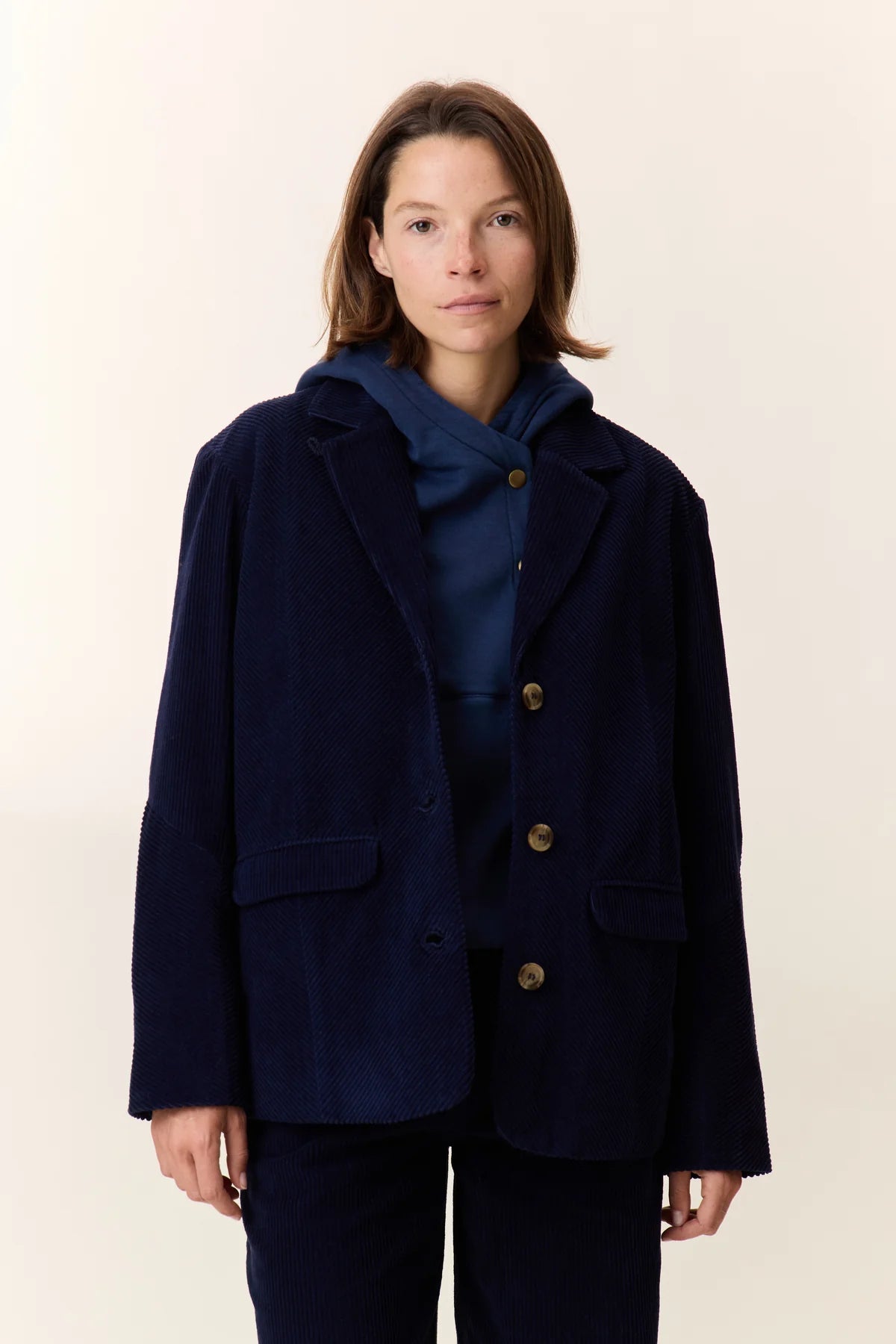 Person wearing a navy blue coat with gold buttons on a white background