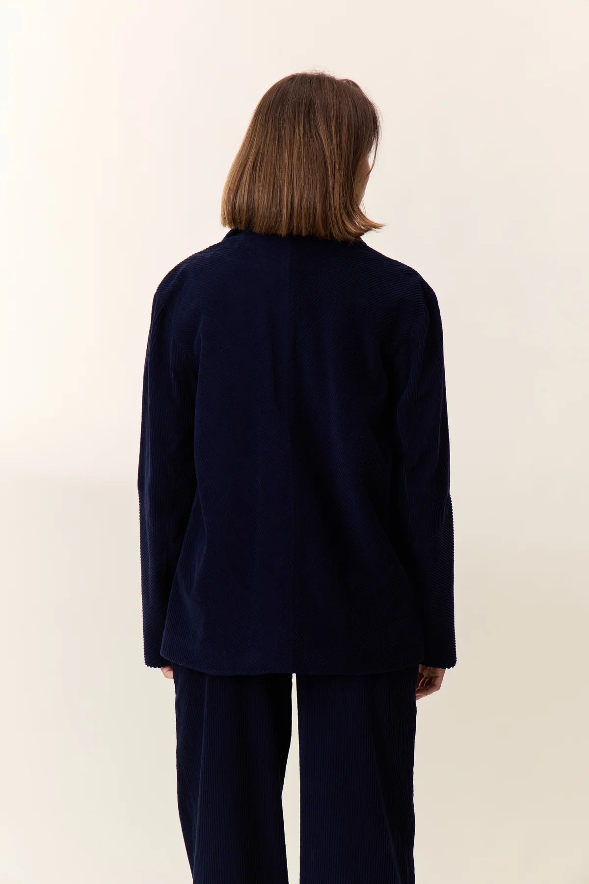 Person wearing a navy jacket and pants on a white background