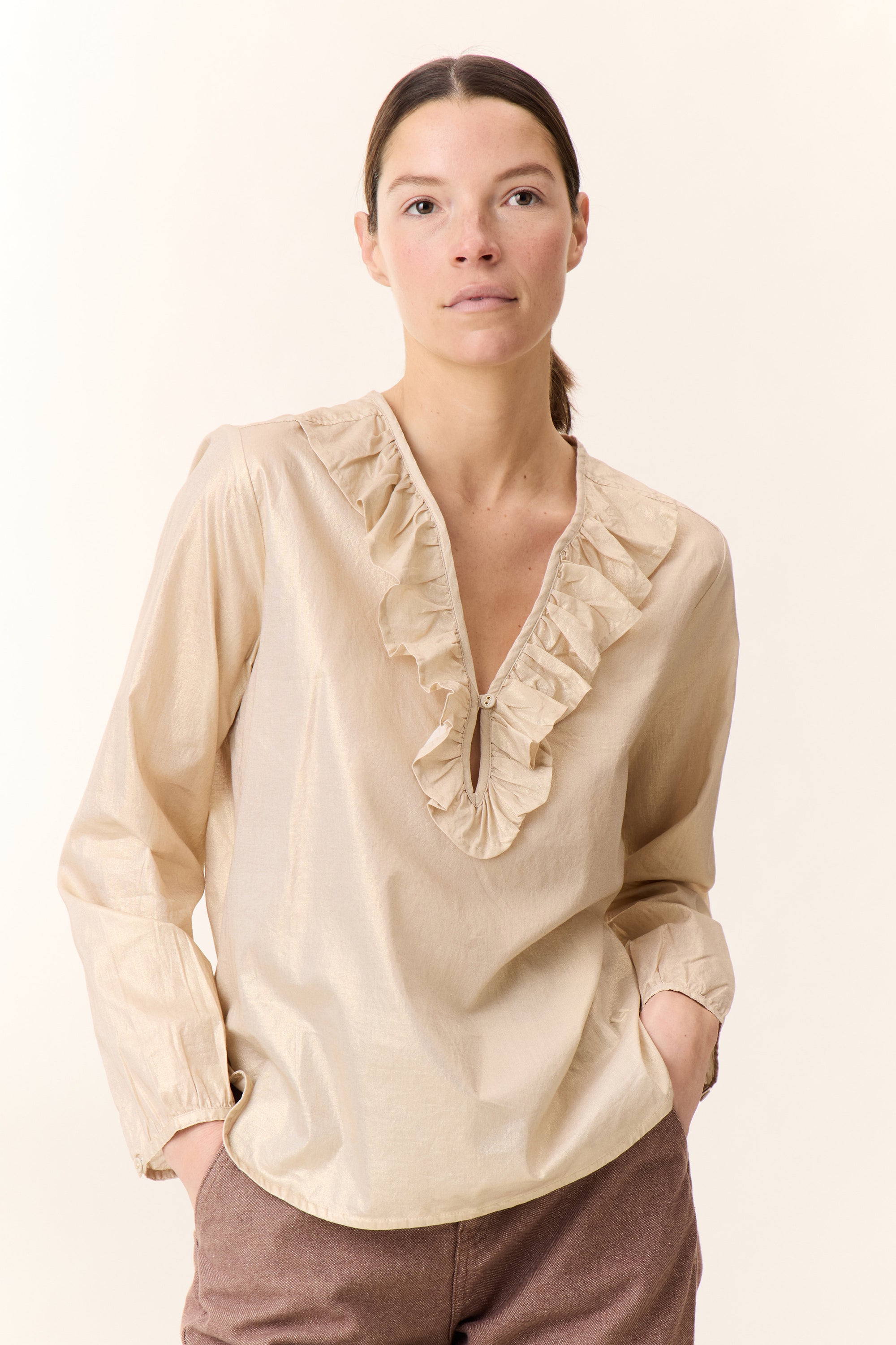 Woman wearing a beige blouse with ruffled details on a plain background