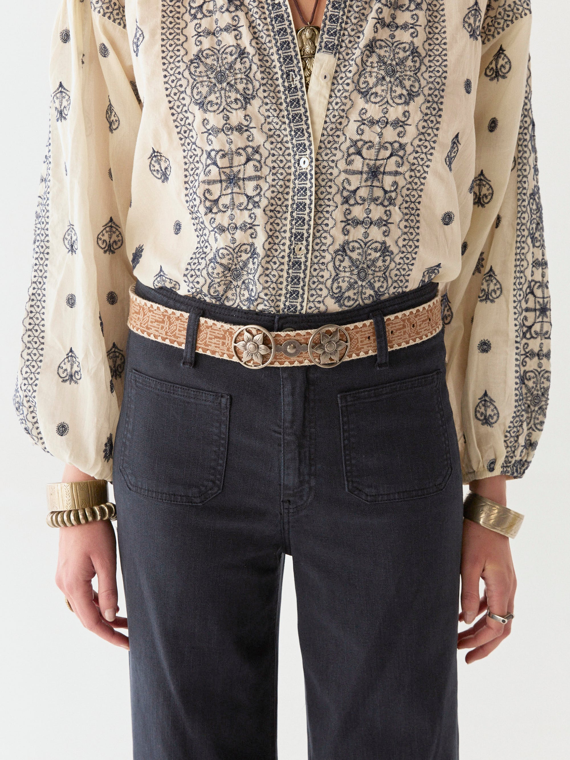 Model wearing navy wide leg pant and cream and navy cotton blouse on a white background.  Paired with tan sandals.  Close up of belt loops of pants and belt. 