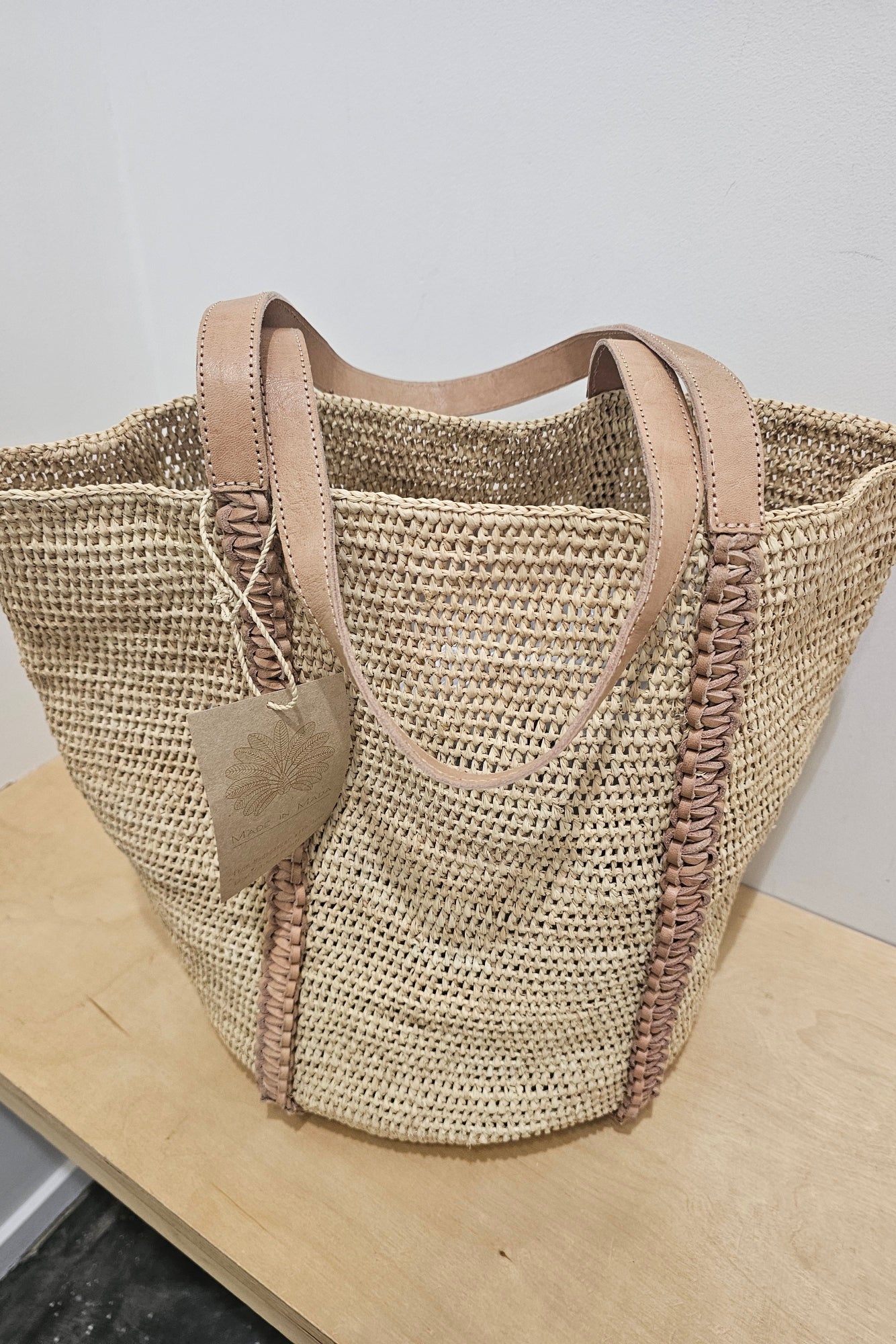 Woven straw natural coloured tote bag with a brown leather handle on a white background