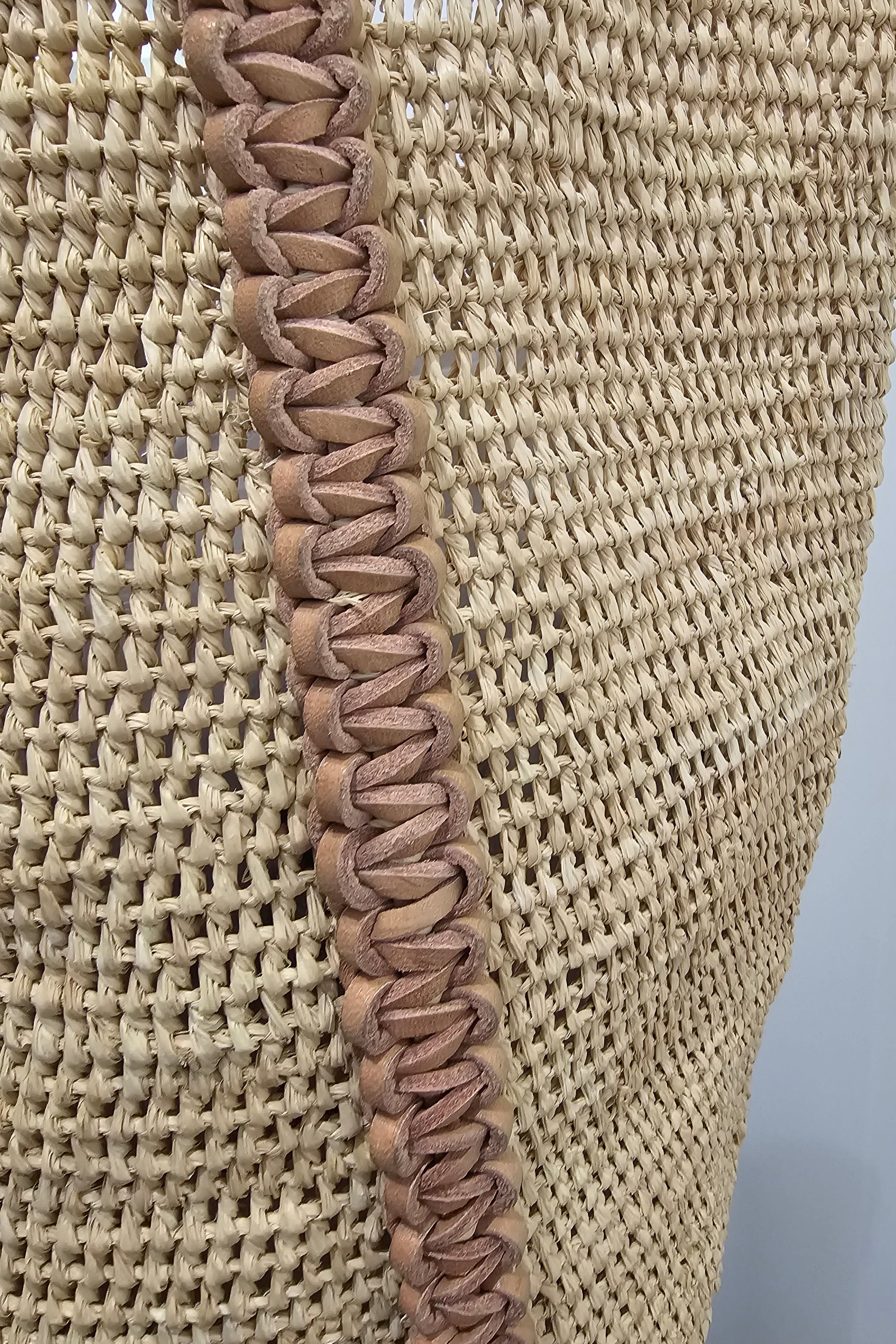 Woven straw natural coloured tote bag with a brown leather handle on a white background