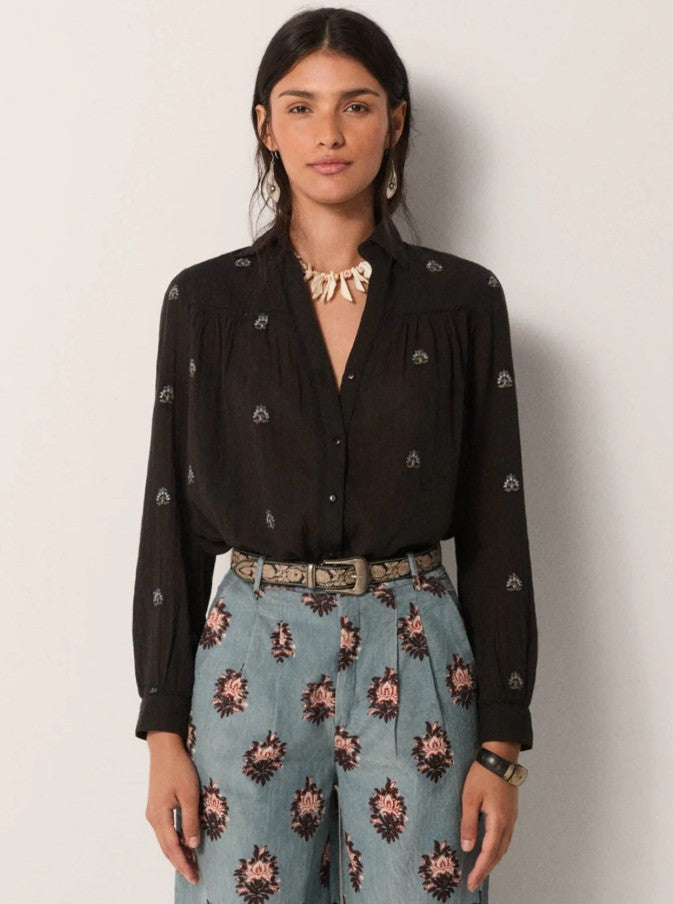 Woman wearing a black blouse with floral patterns and blue pants with floral patterns against a plain background