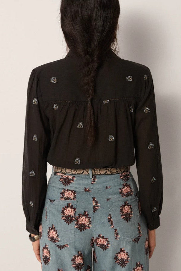 Person wearing a black floral blouse and patterned pants against a plain background