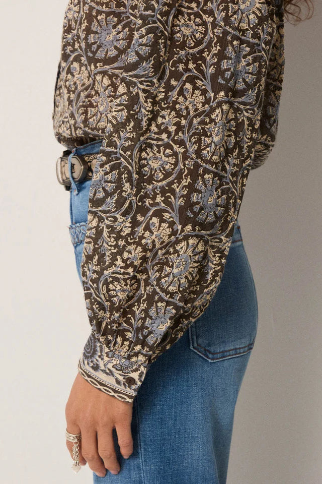 Woman wearing a patterned blouse and blue jeans against a plain background