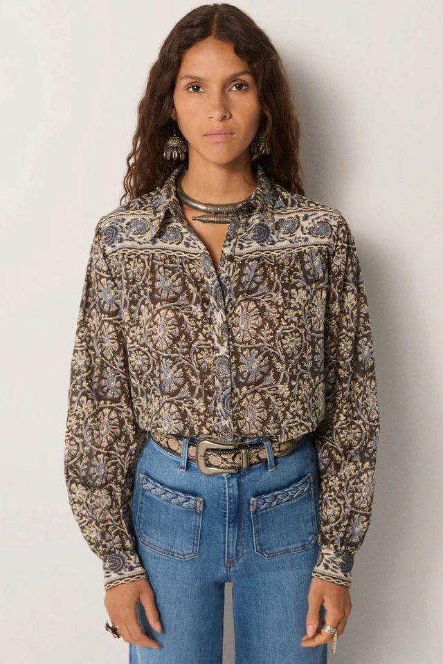 Woman wearing a patterned blouse and blue jeans against a plain background