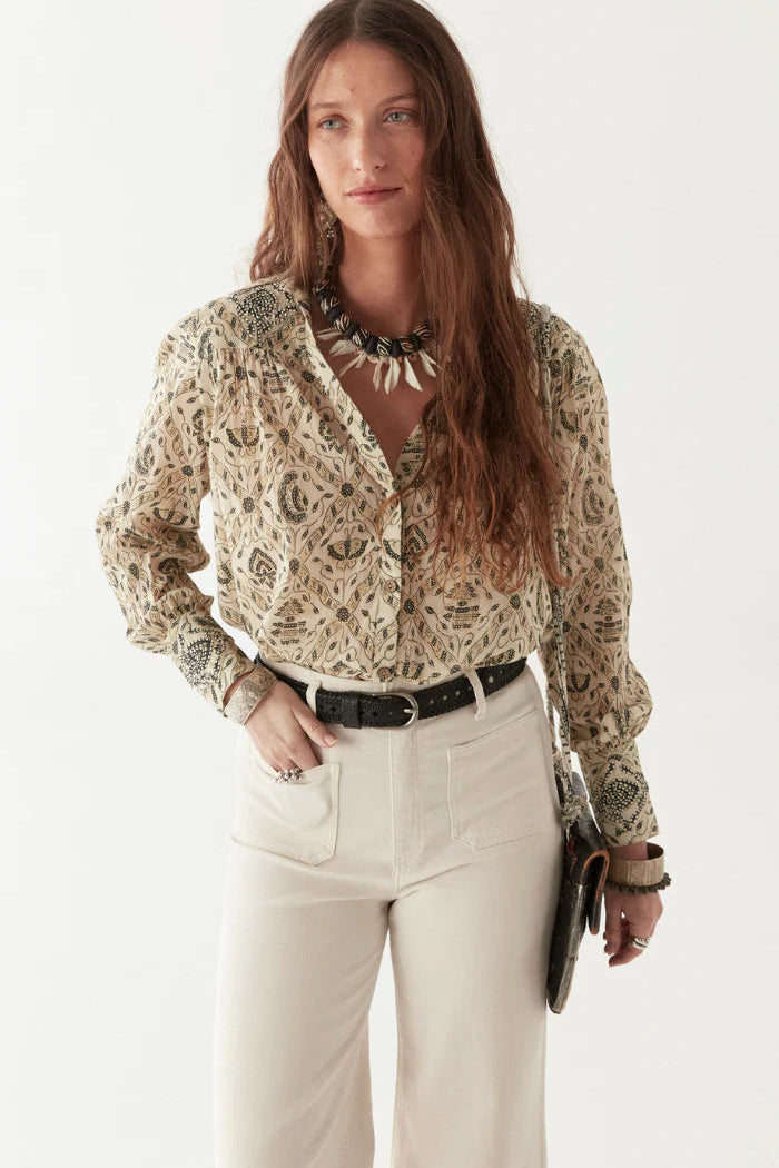 Woman wearing a patterned blouse with a plain background paired with white jeans and black belt. 