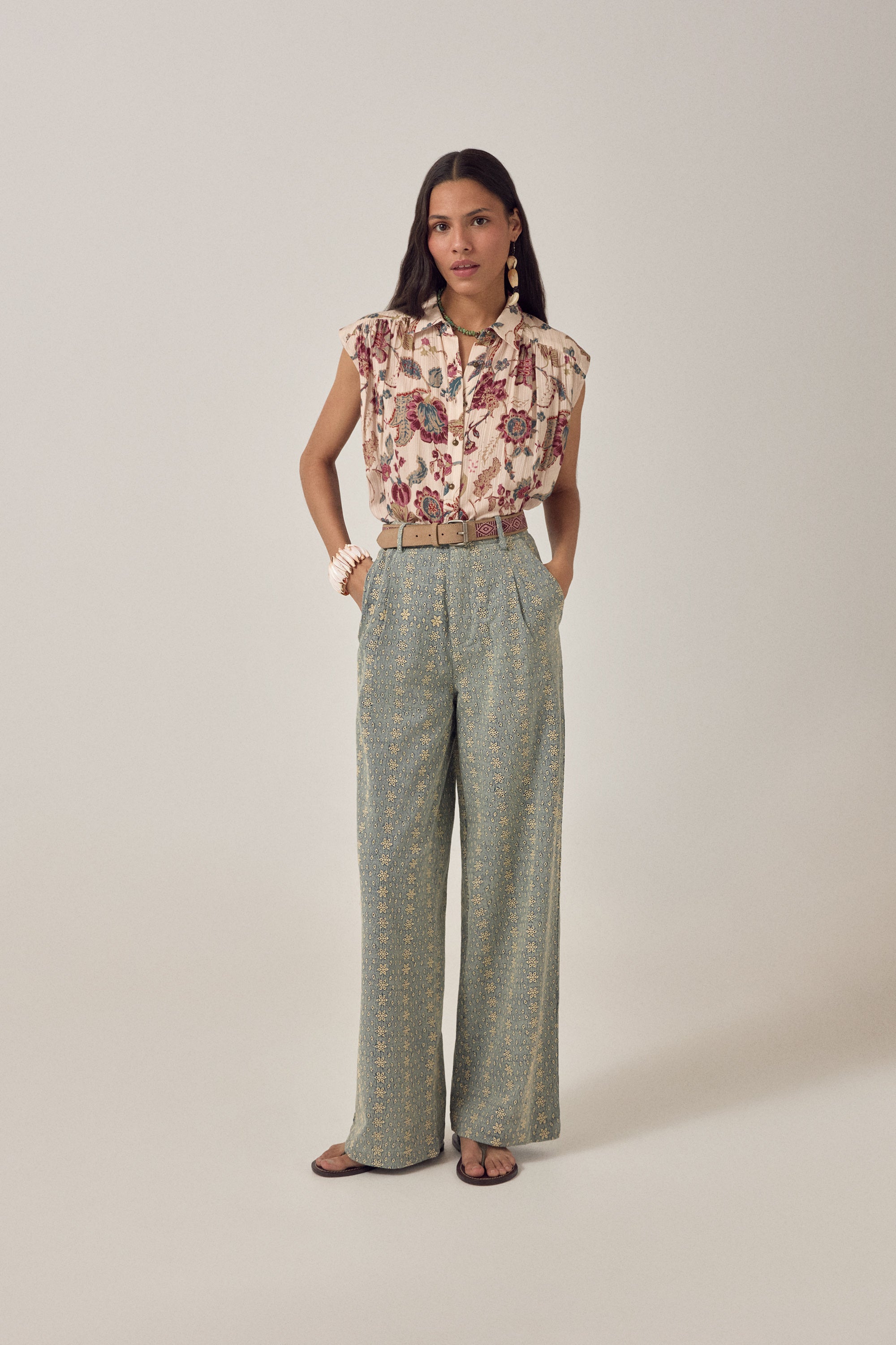 Woman wearing a short sleeve floral blouse with patterned pants on a plain background
