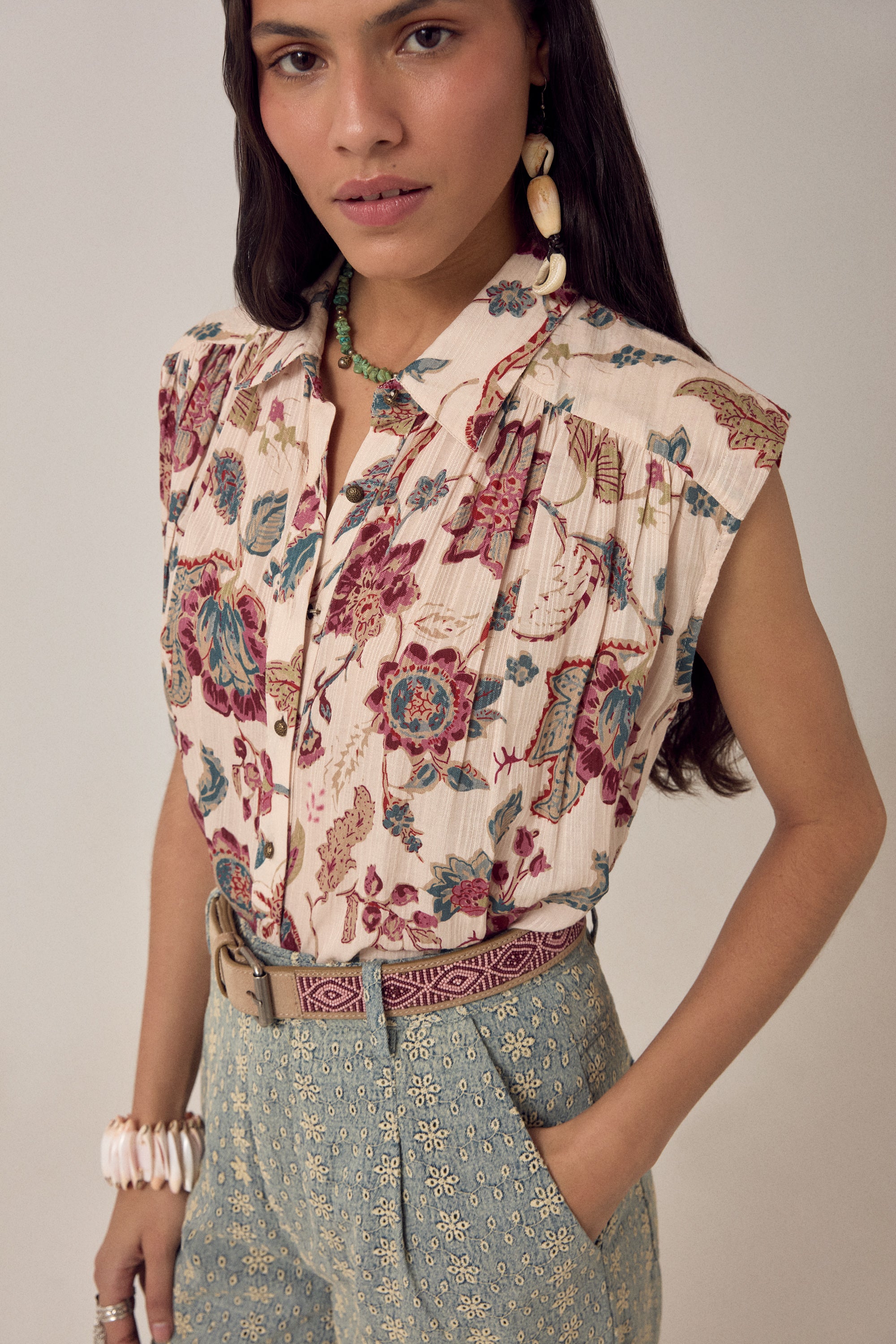Woman wearing a short sleeve floral blouse with patterned pants on a plain background