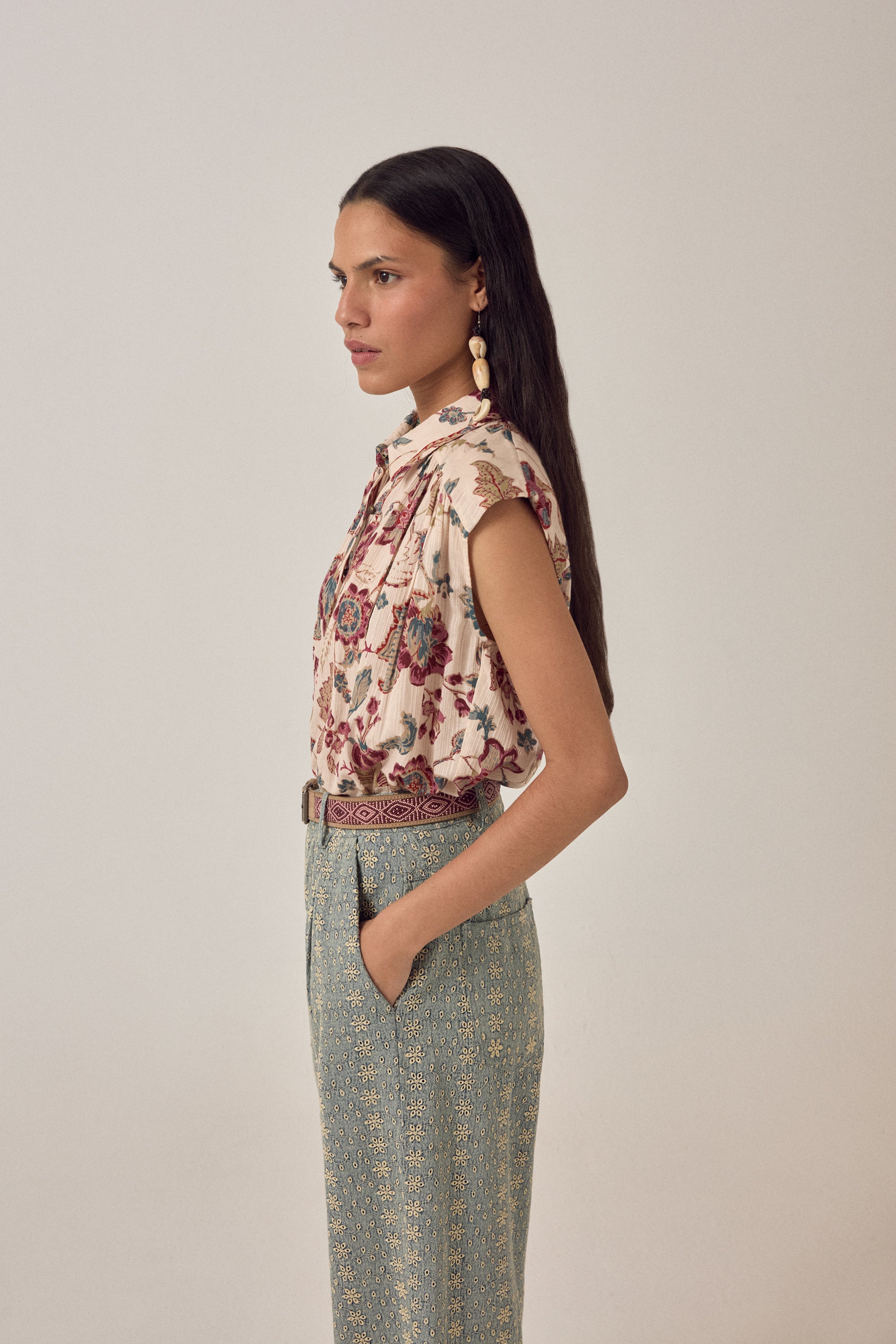 Woman wearing a short sleeve floral blouse with patterned pants on a plain background