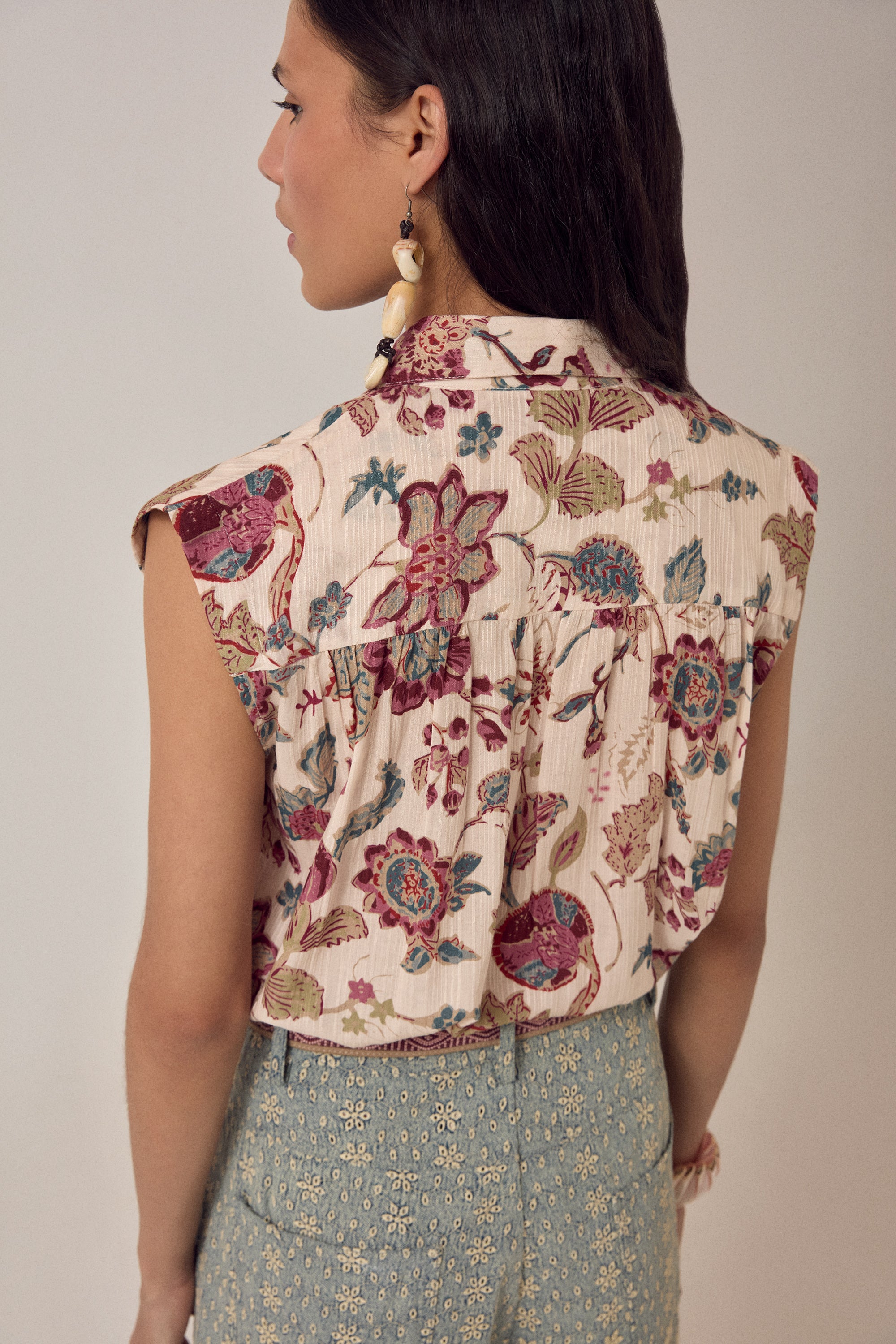 Woman wearing a short sleeve floral blouse with patterned pants on a plain background