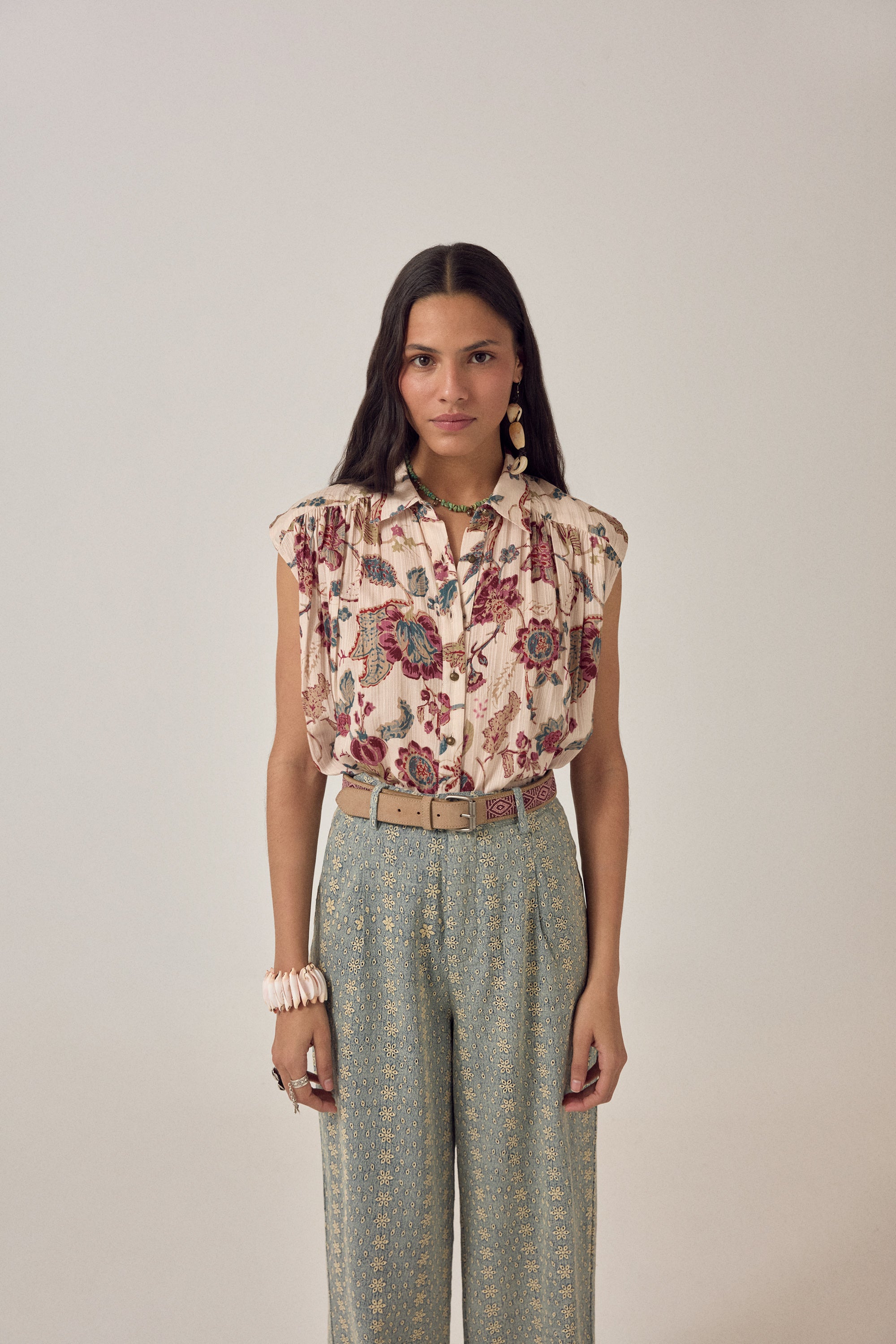 Woman wearing a short sleeve floral blouse with patterned pants on a plain background