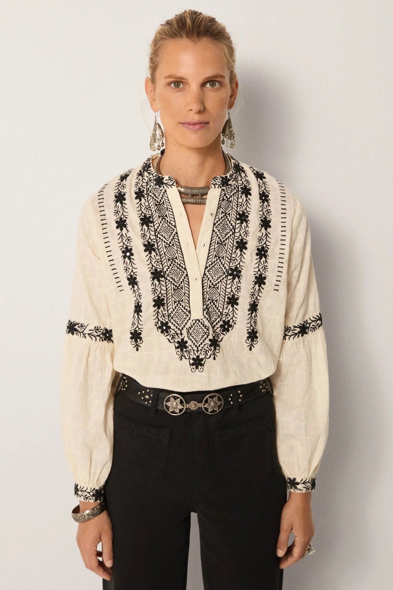 Woman wearing a cream embroidered blouse with black patterns on a plain background